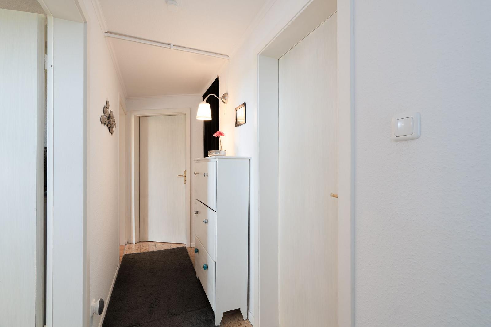 Hallway with white doors, cabinet, and wall lamp. Dark rug on the floor.