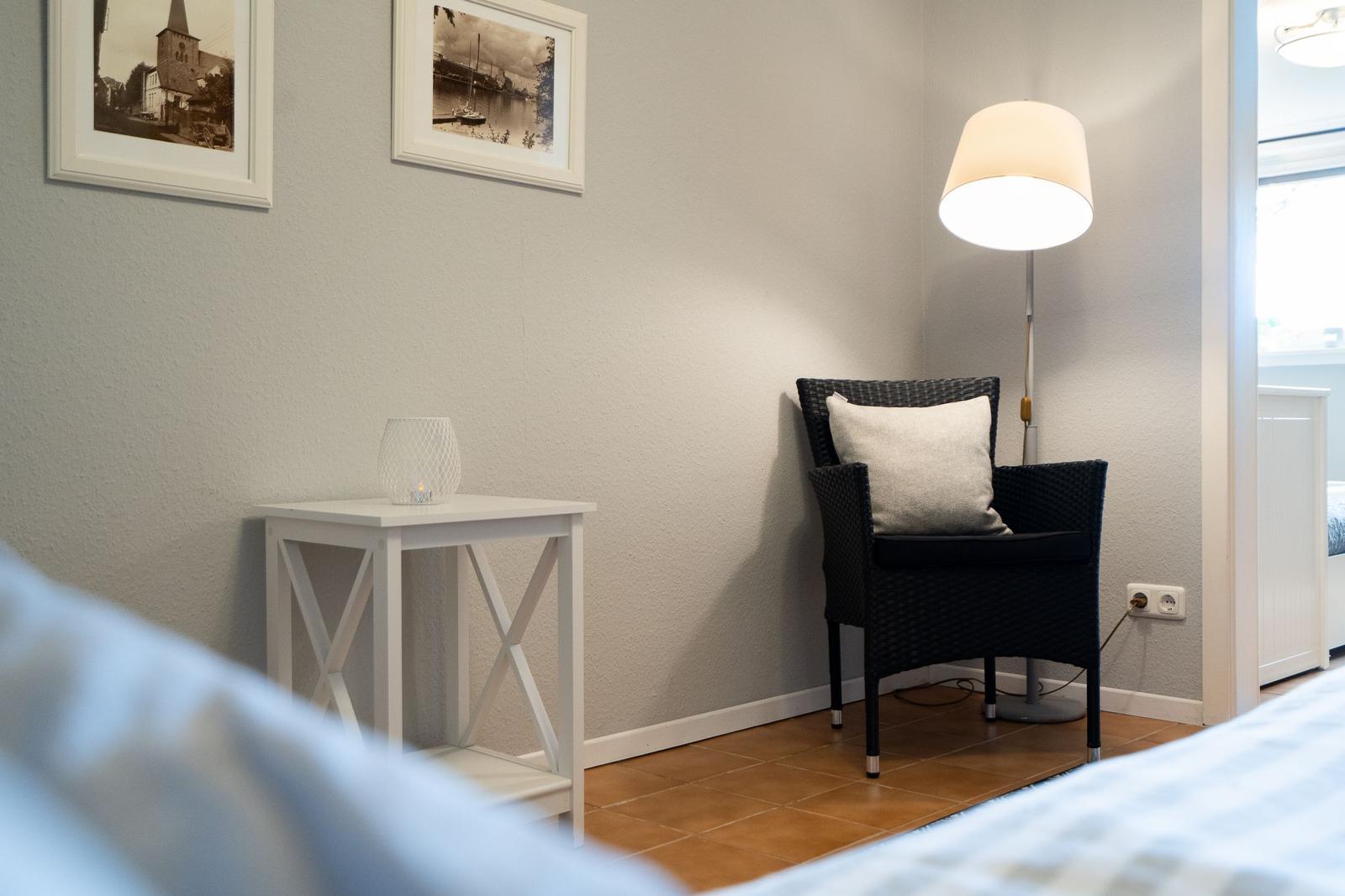 Black chair with pillow, floor lamp, and table with candle against wall with pictures.