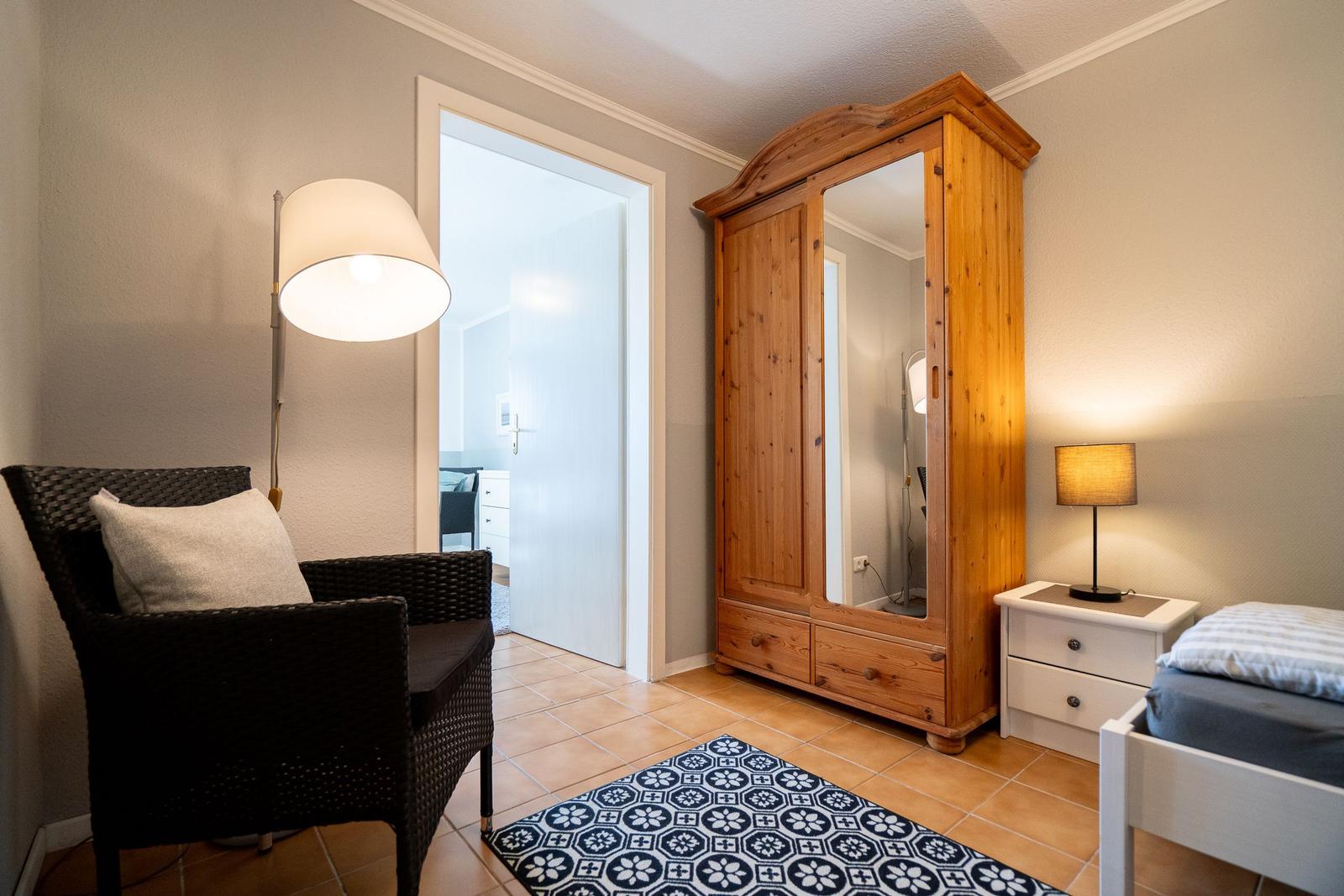 Bedroom with wooden wardrobe, bed, nightstand, and armchair.