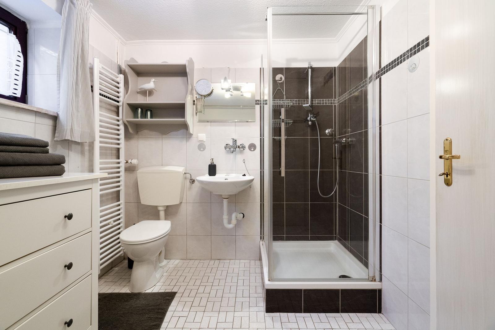 Bathroom with shower, sink, and toilet. White tiles and dark accents.