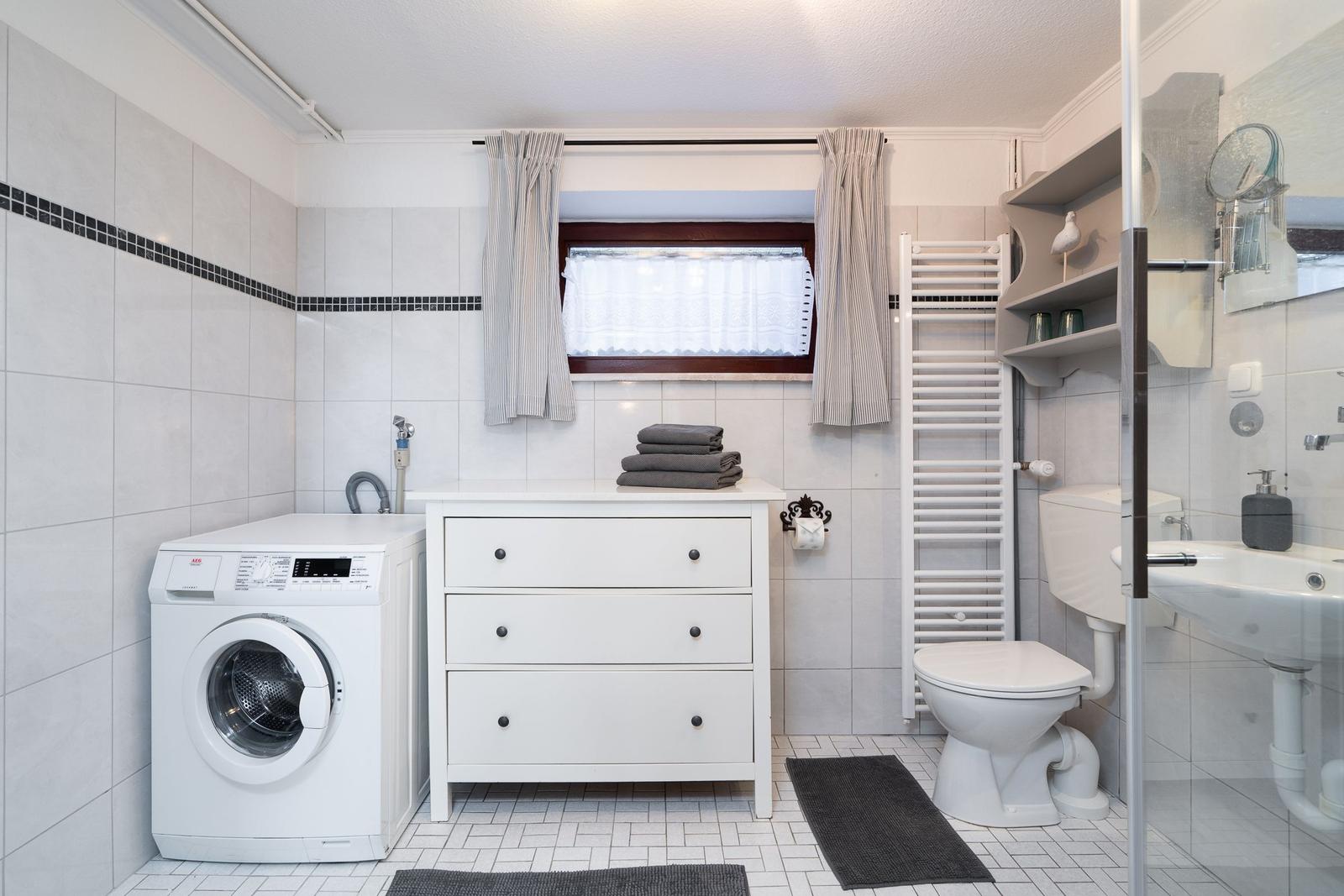 Bathroom with washing machine, sink, toilet, and window with curtains.