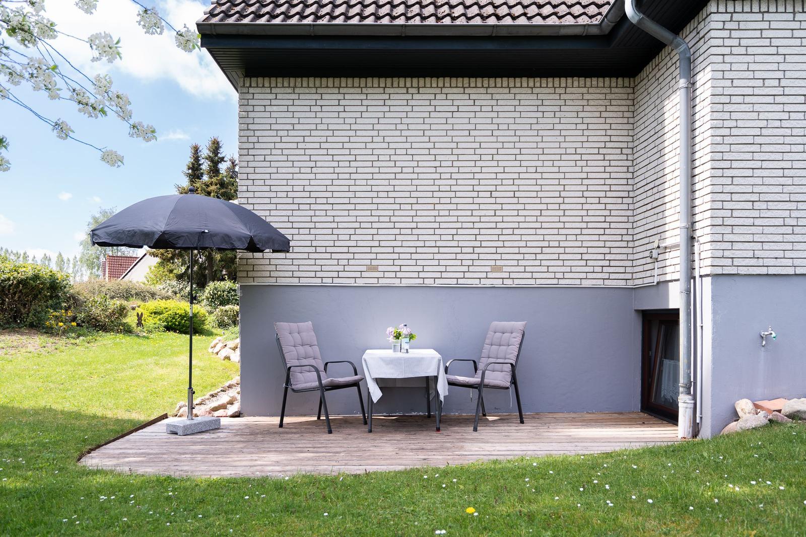 Terrace with table, two chairs, and umbrella in front of white brick wall.