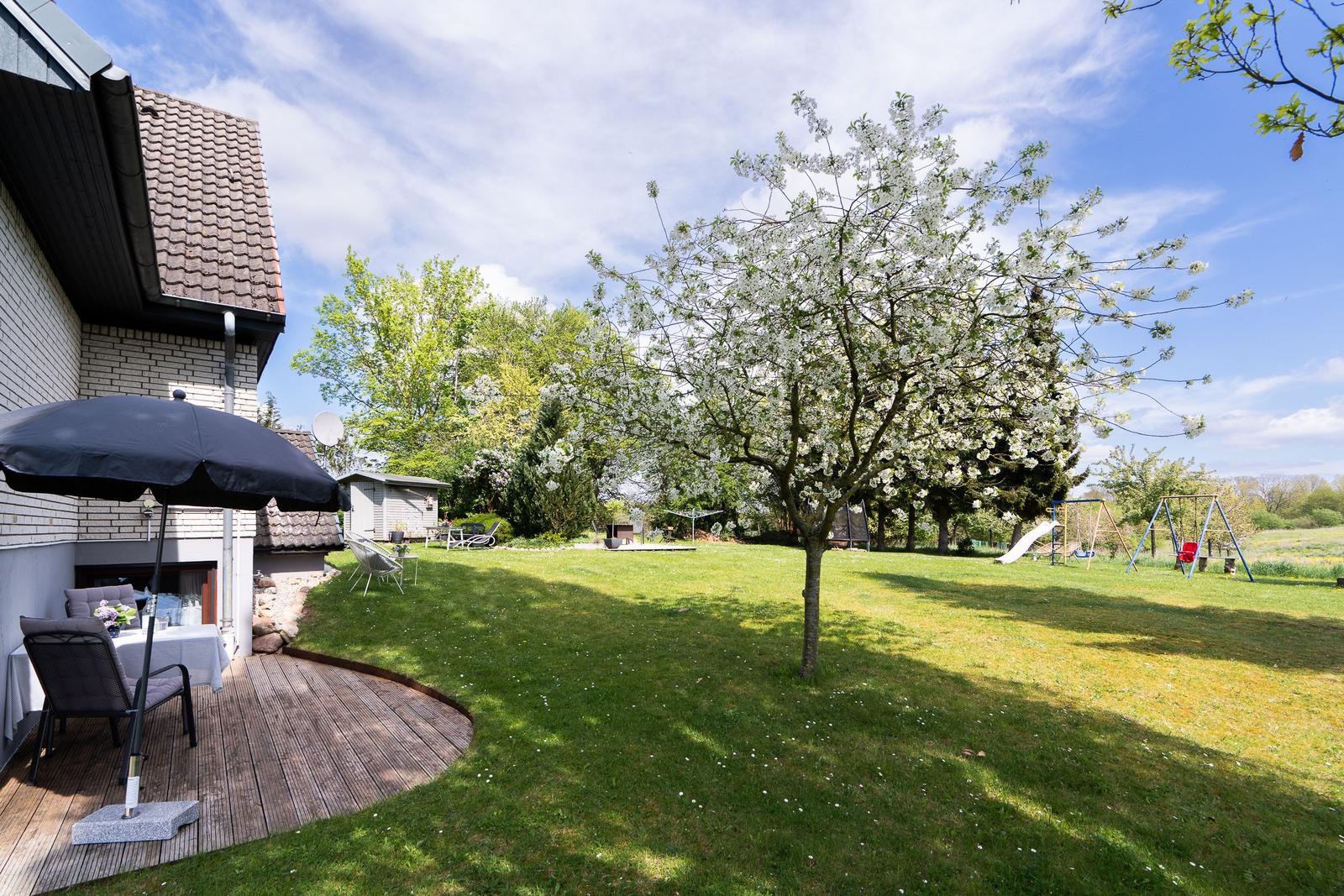 House with terrace, flowering tree, and playground in the garden.