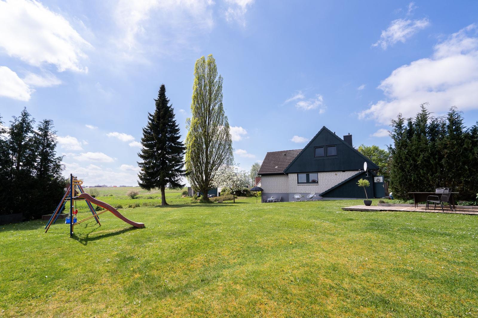 House with large garden, playground, and terrace under blue sky.