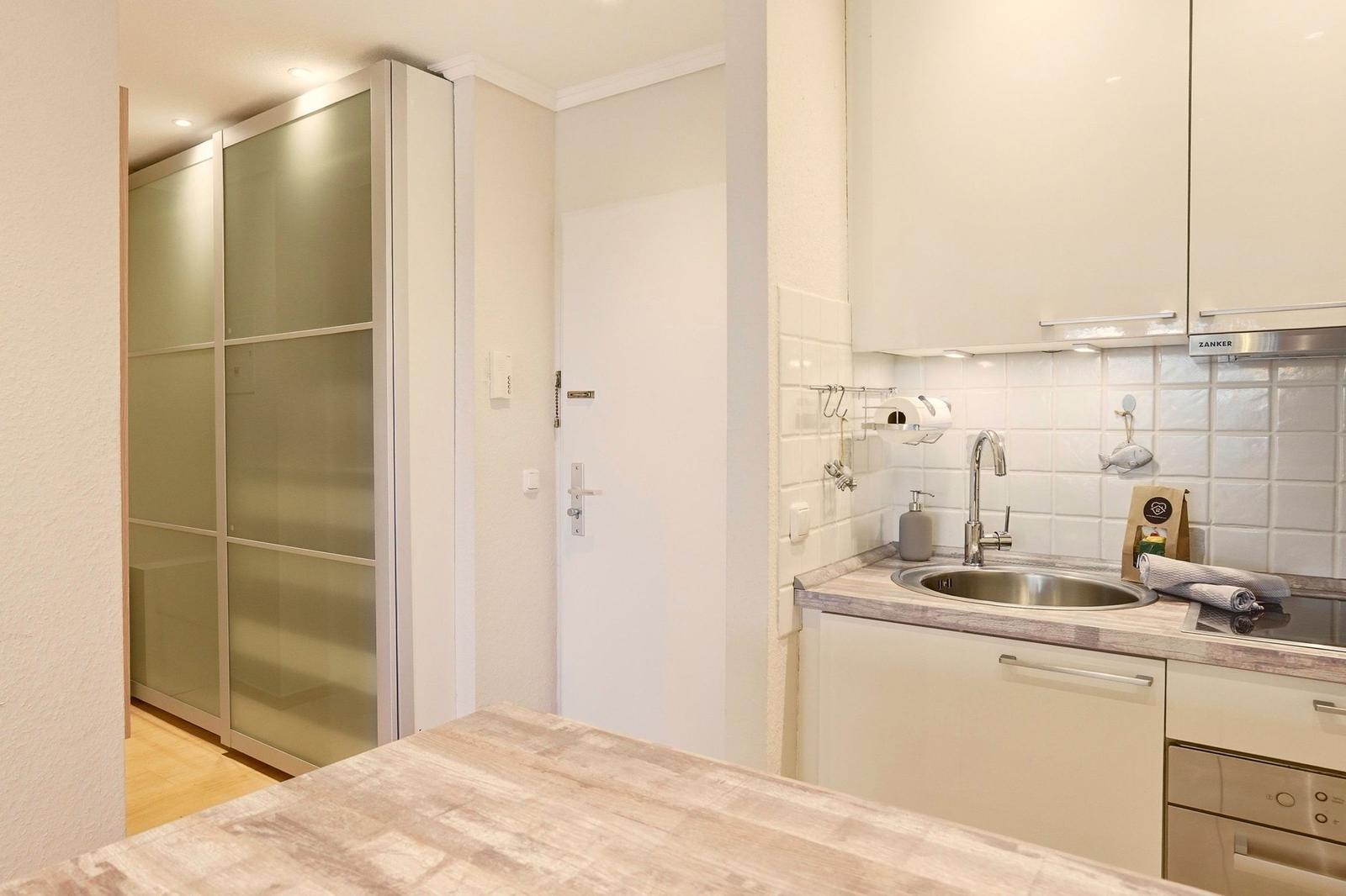 Küche mit Spüle, Arbeitsplatte und Schränken. Im Hintergrund ist ein Schlafzimmer mit Schiebetüren.