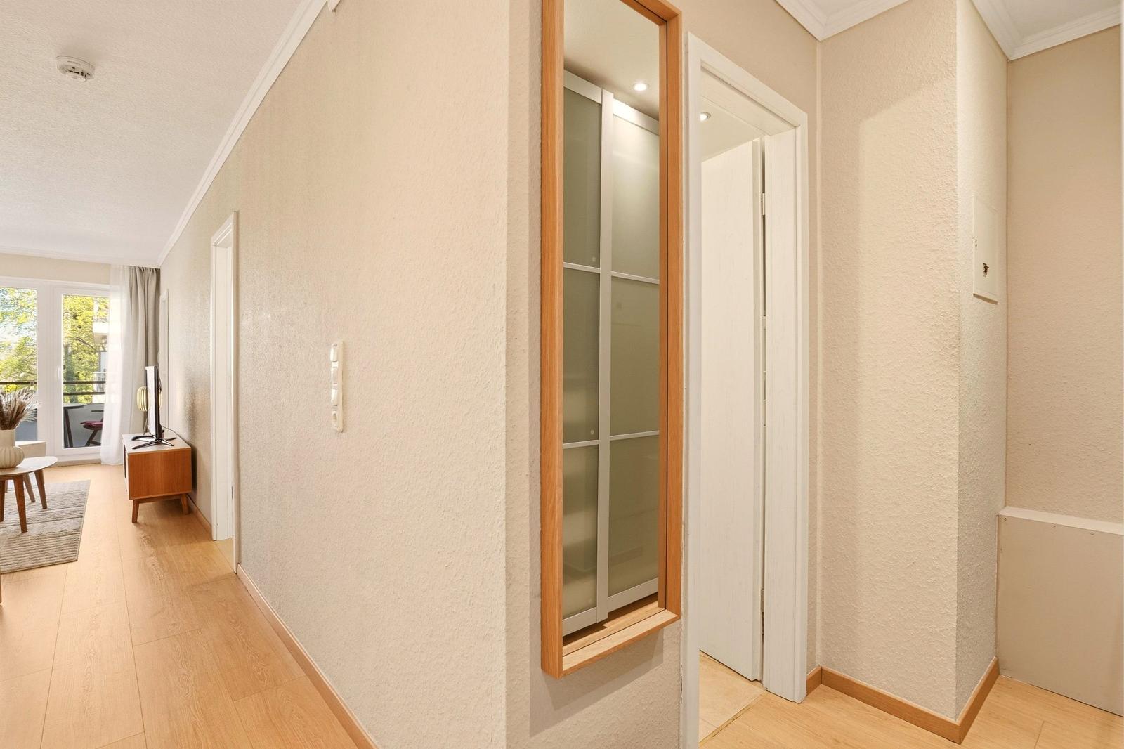 Flur mit Holzboden, Schiebetüren und Blick in Wohnbereich mit Balkon.