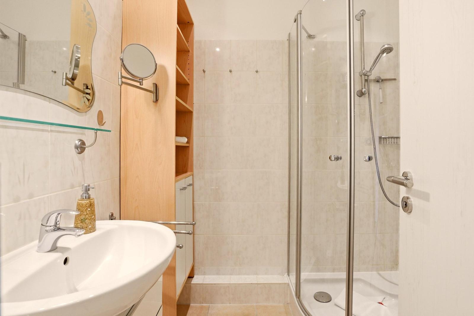 Badezimmer mit Dusche, Waschbecken und Holzregal