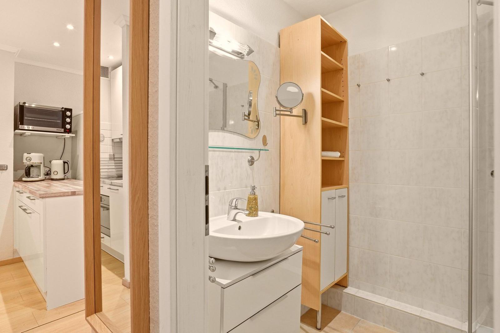 Badezimmer mit Waschbecken, Spiegeln und Dusche. Küche mit Küchenzeile und Geräten sichtbar.