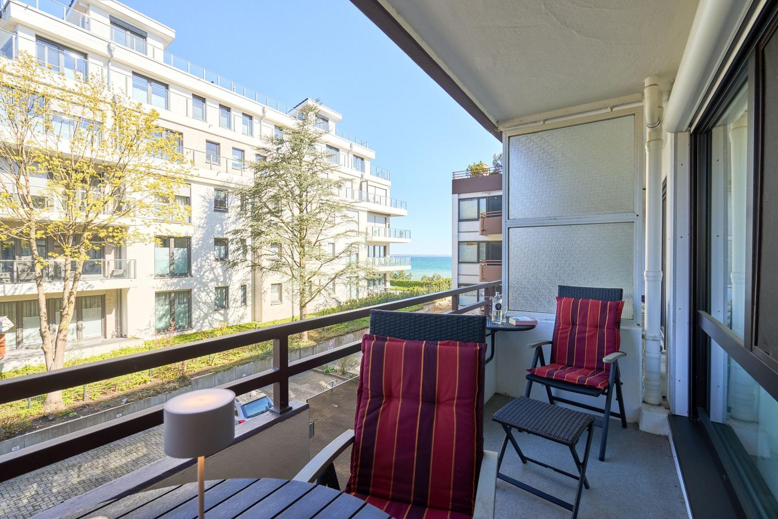 Terrasse mit zwei Stühlen und Tisch. Blick auf Gebäude und Meer.