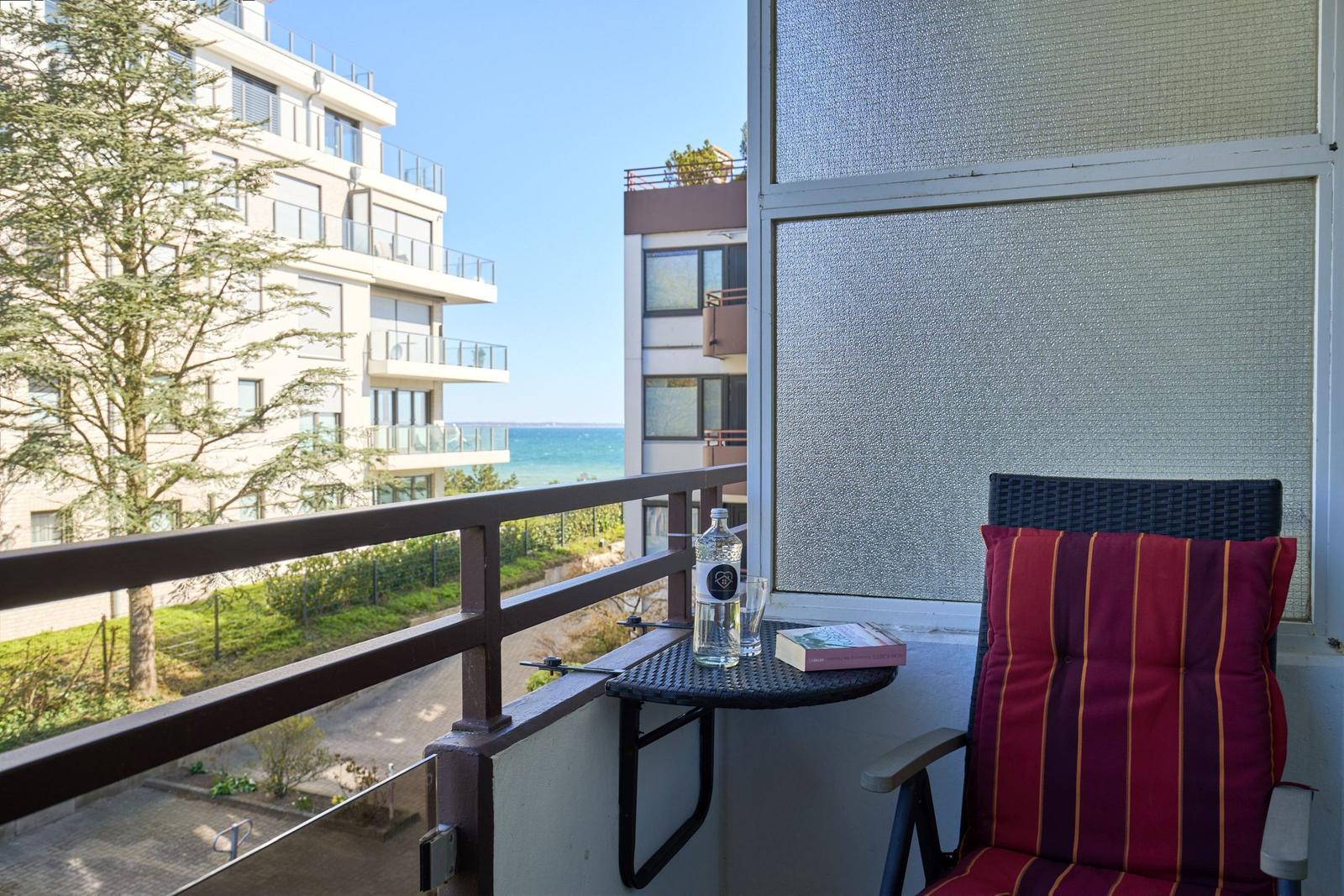 Balkon mit Stuhl und Tisch, Blick auf Meer und Gebäude.