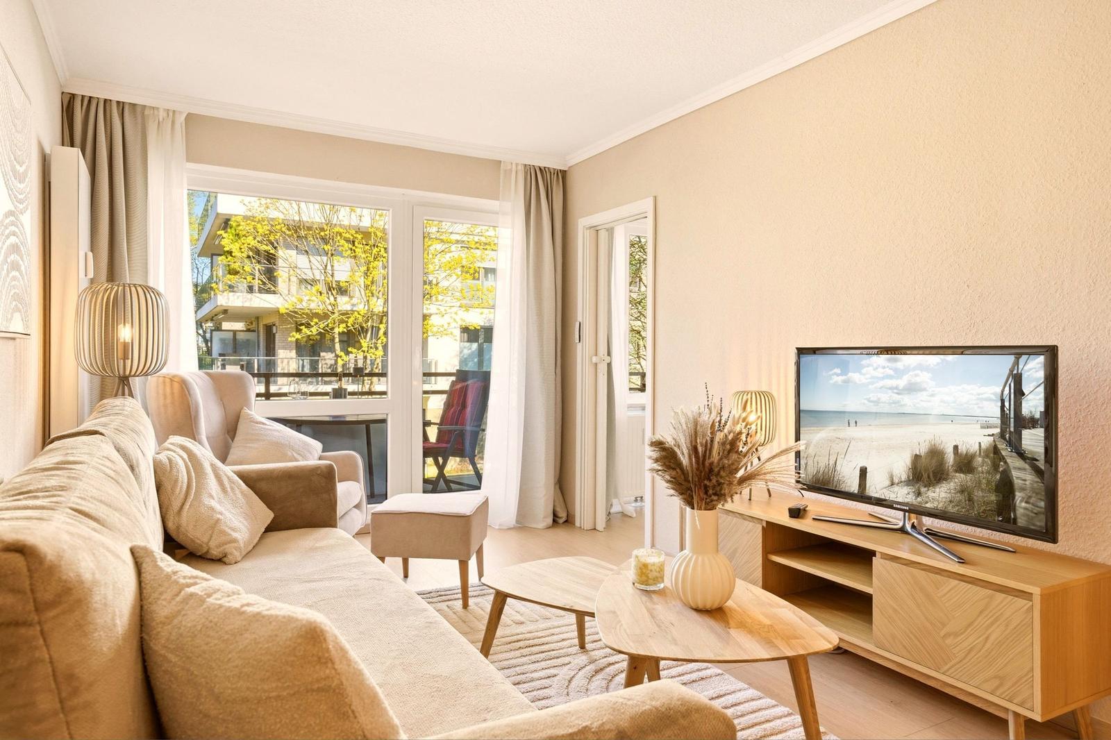 Wohnzimmer mit Sofa, Fernseher und Blick auf Balkon.