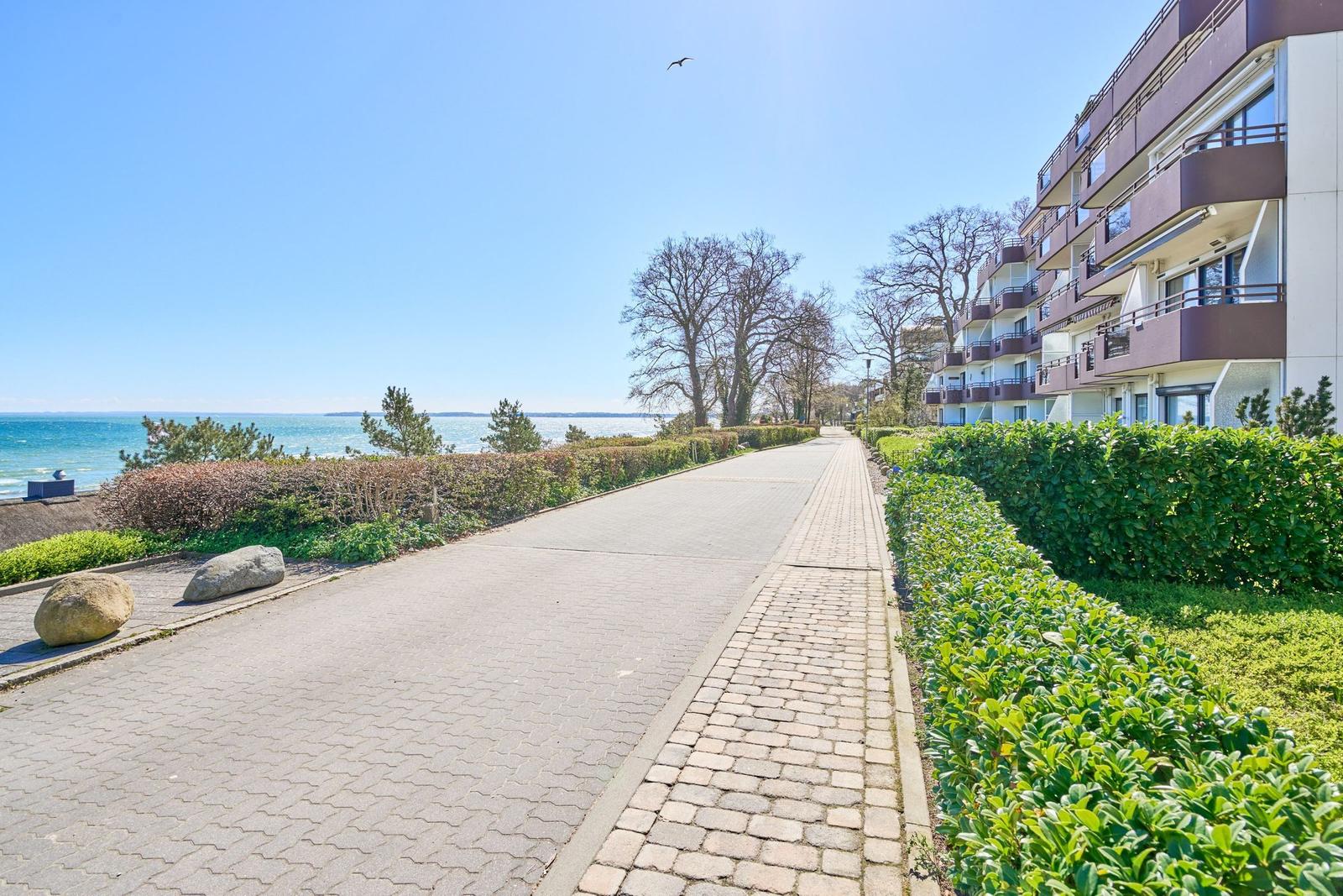 Pfad entlang des Meeres mit Wohnhaus und Grünflächen.