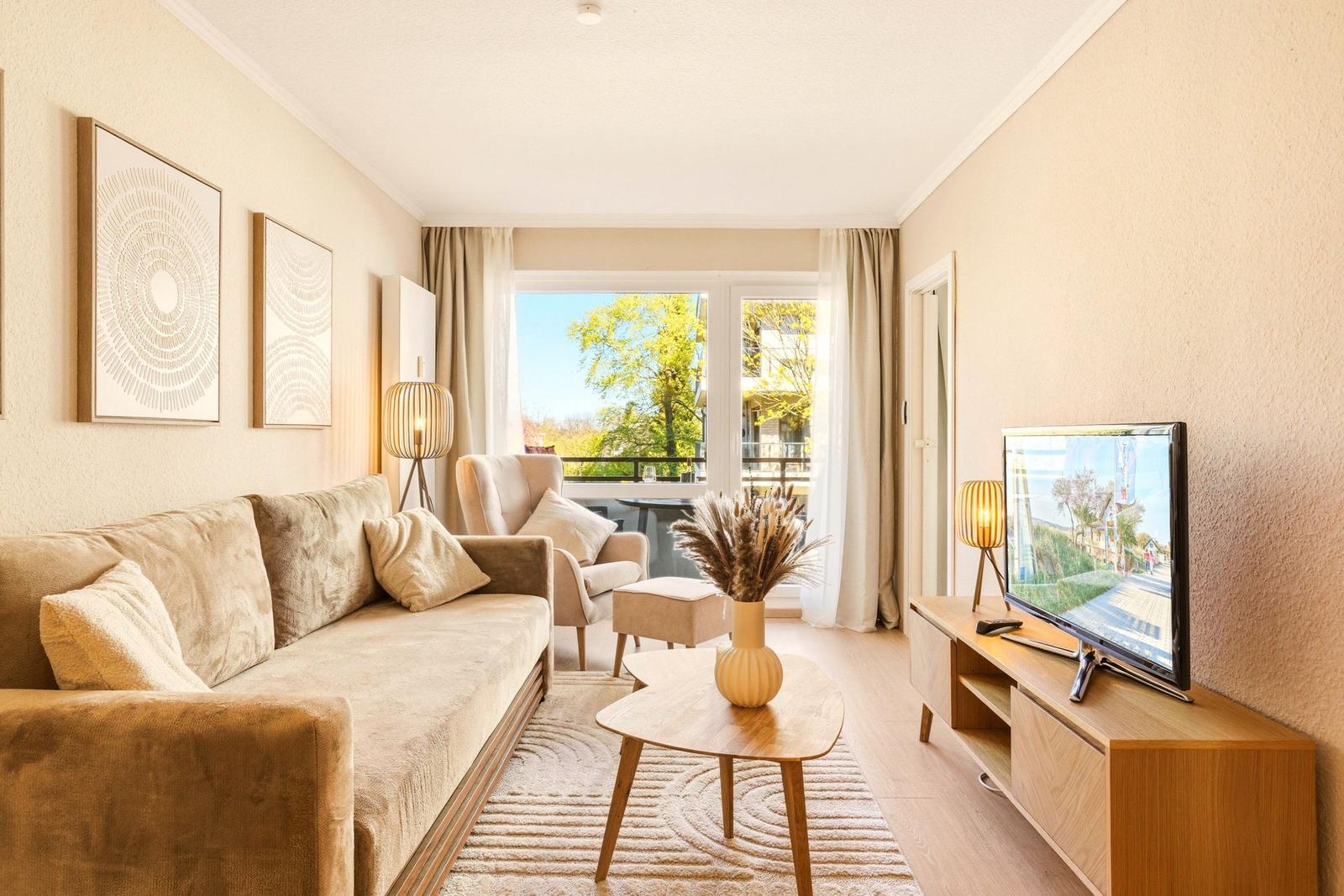 Wohnzimmer mit Sofa, Couchtisch und TV. Balkon mit Blick auf Bäume.