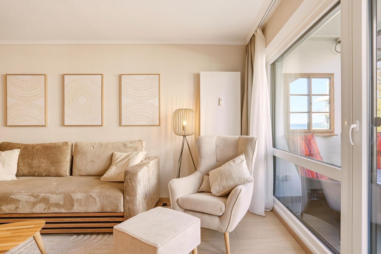 Wohnzimmer mit Sofa, Sessel und Glasfront zum Balkon.