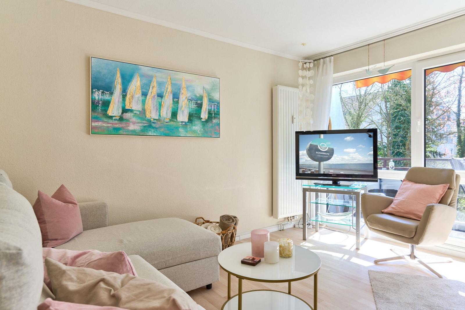 Wohnzimmer mit Sofa, Sessel und Fernseher. An der Wand hängt ein großes Bild mit Segelbooten.