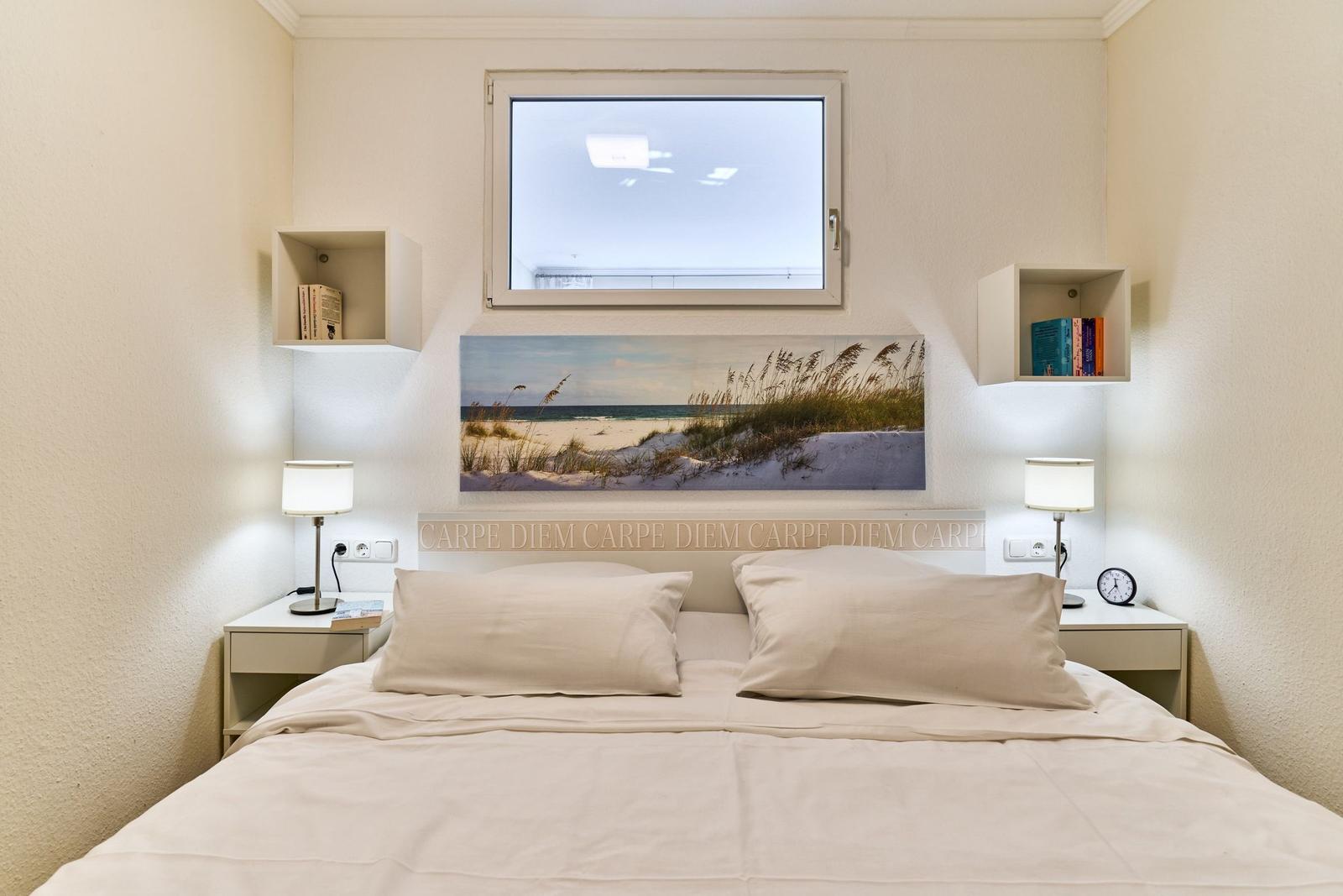Schlafzimmer mit Bett, Nachttischen und Wandbild. Fenster und Regale sind sichtbar.