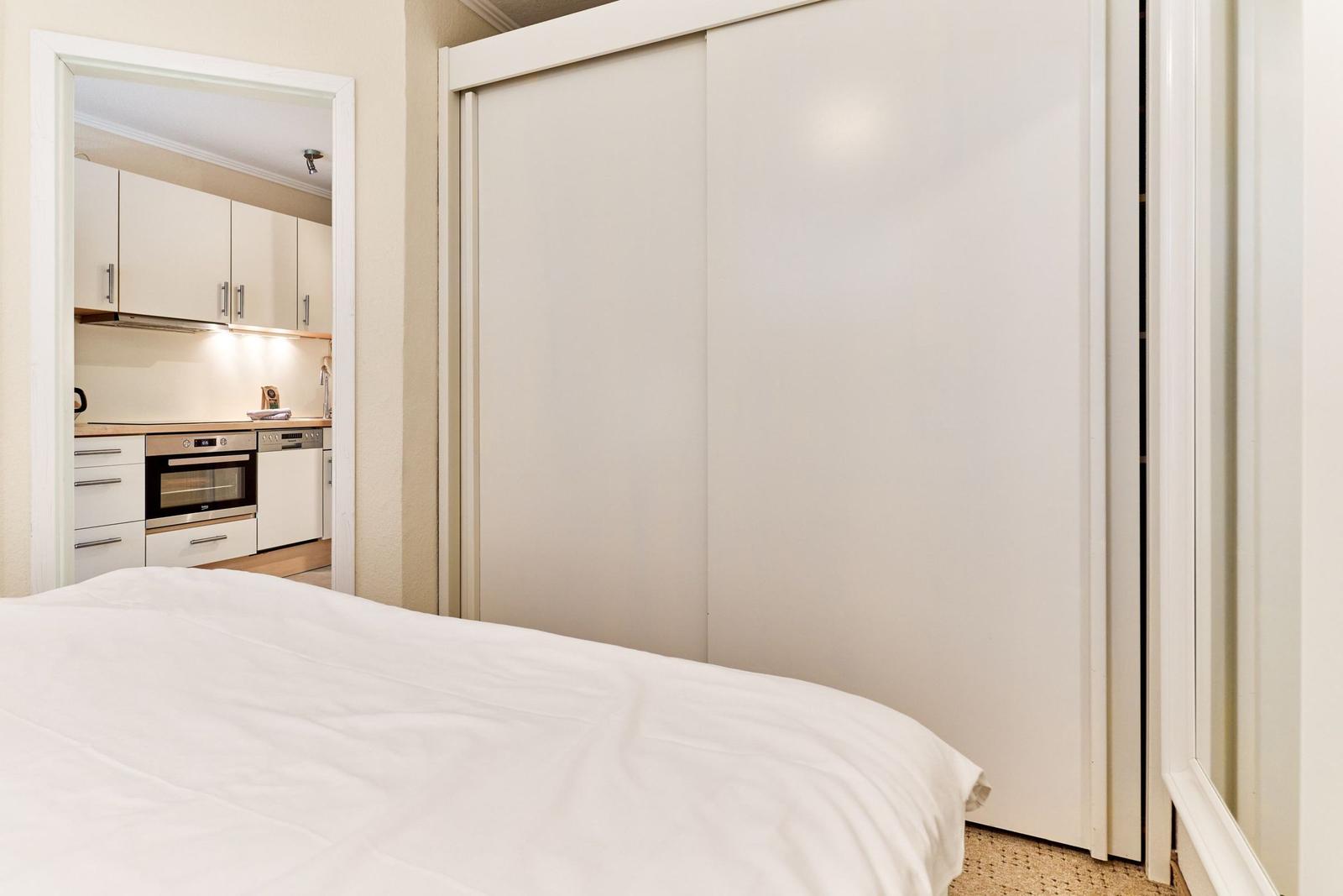 Schlafzimmer mit Bett und Schwebetürenschrank. Küche mit Arbeitsplatte und Backofen sichtbar.