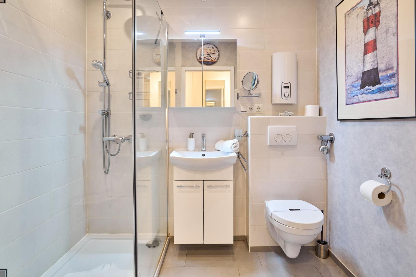 Badezimmer mit Dusche, Waschbecken und Toilette. Wandbild mit Leuchtturm.