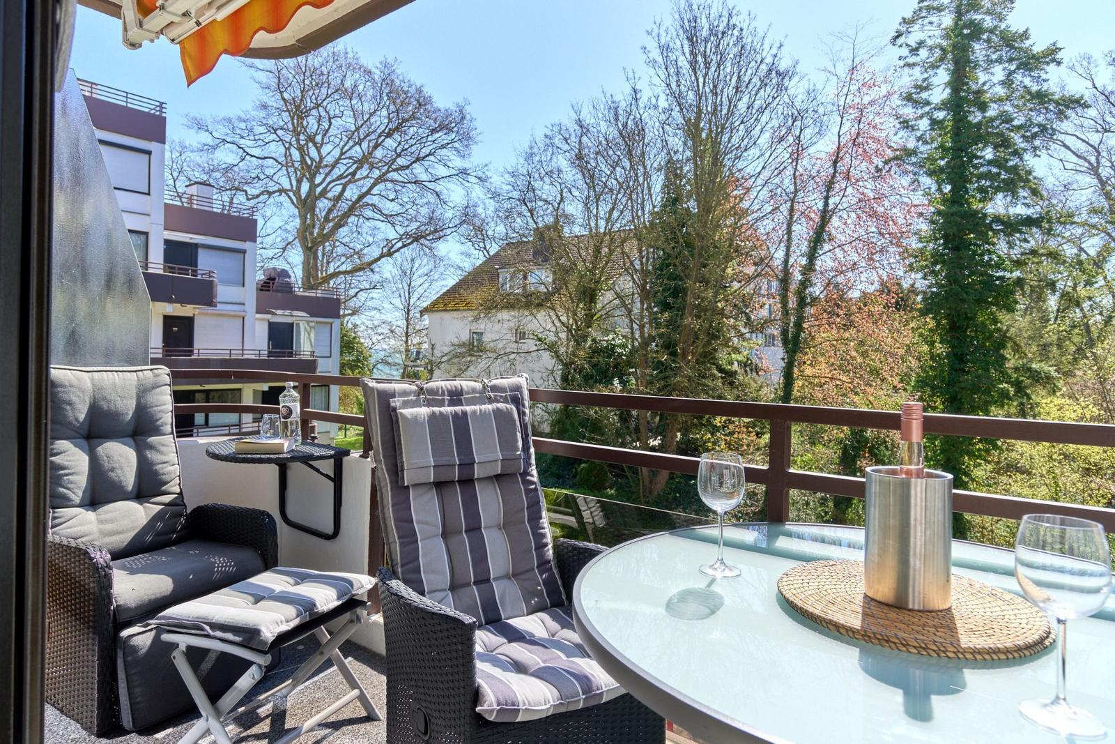 Terrasse mit Sitzgruppe, Tisch und Blick auf Bäume und Gebäude.