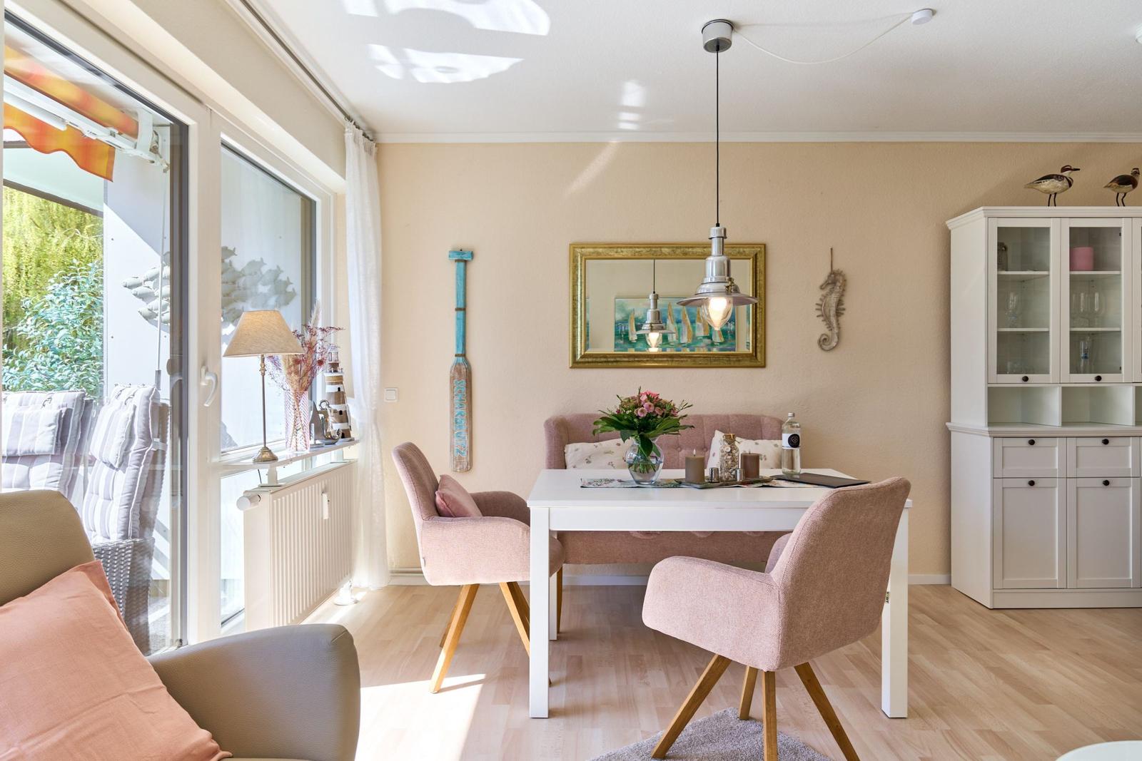 Esszimmer mit weißem Tisch, rosa Stühlen und Glaswand. Fensterblick auf Terrasse.