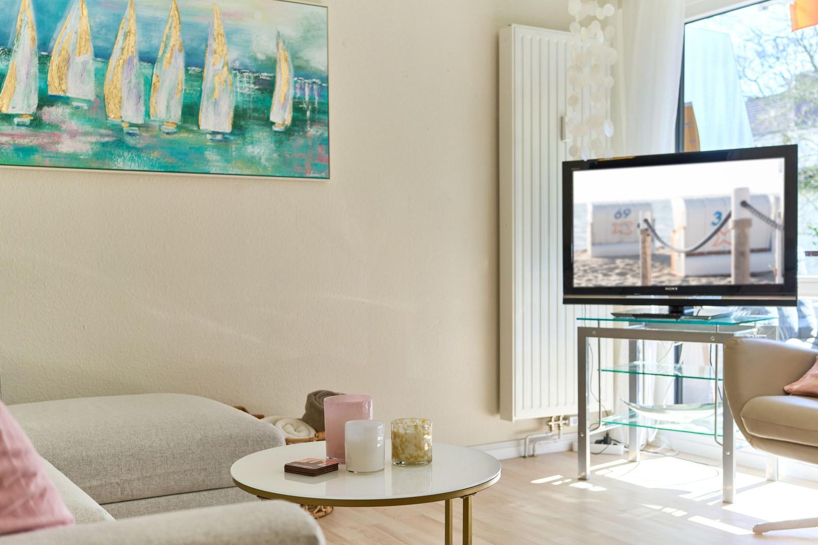 Wohnzimmer mit Sofa, Fernseher und Wandbild mit Segelbooten.