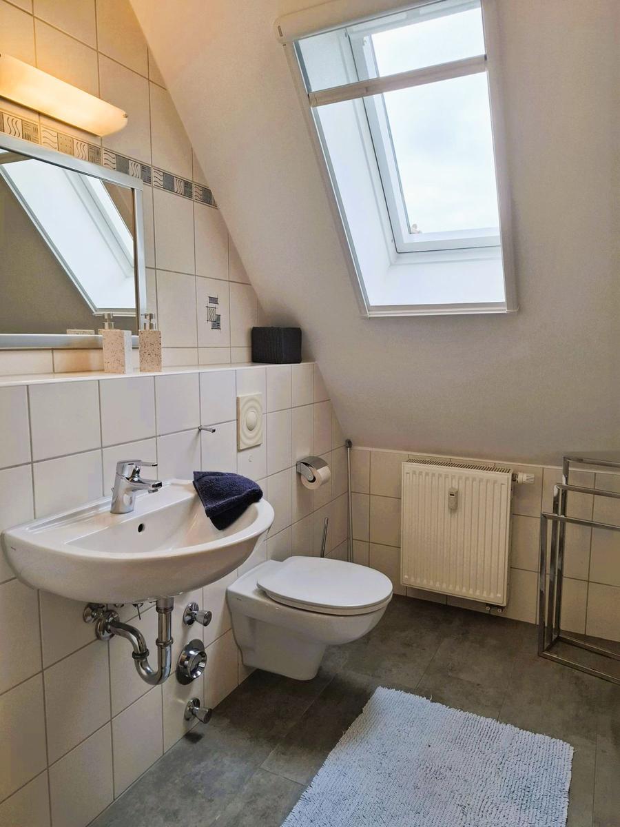 Badezimmer mit Waschbecken, Toilette und Dachfenster. Fliesenwand und Heizkörper.