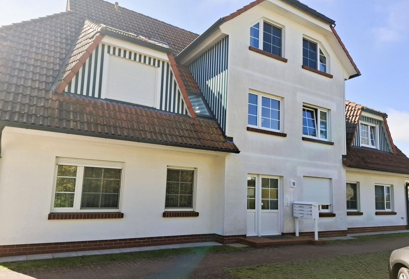 Modernes Einfamilienhaus mit weißen Wänden und braunem Dach. Vordere Tür mit Briefkasten.