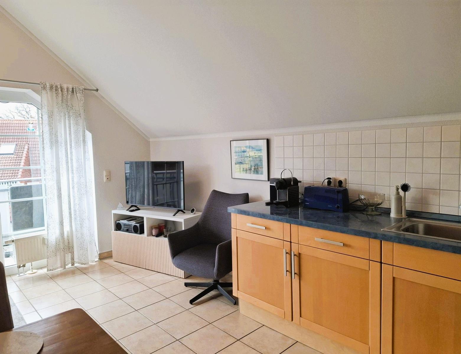 Wohnküche mit TV, Stuhl und Küchenzeile unter schräger Decke.