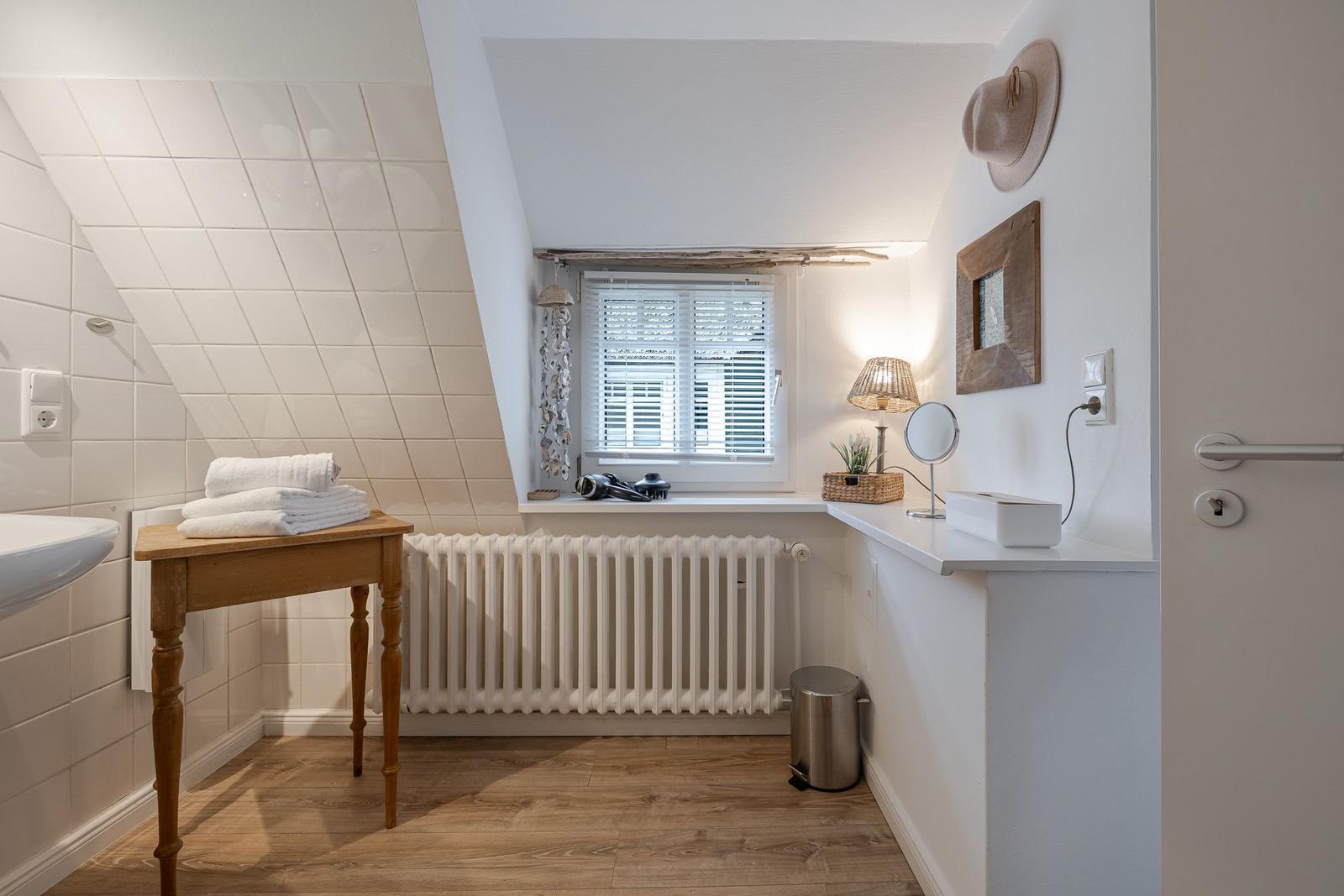 Badezimmer mit Holztisch, Fenster, Heizung und Wanddekoration.