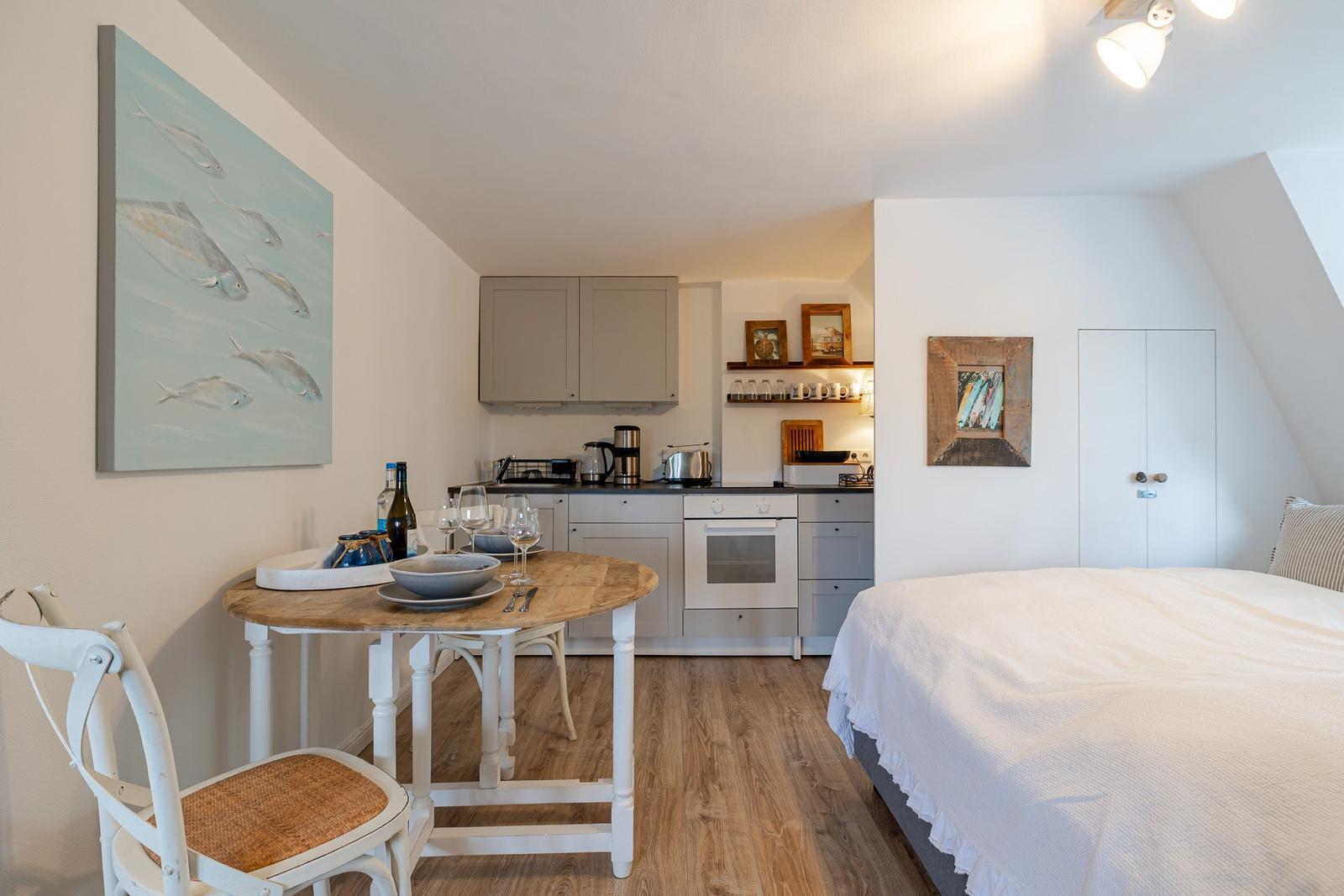 Schlafzimmer mit kleiner Küche und Esstisch. Holzboden und Wandbild mit Fischen.