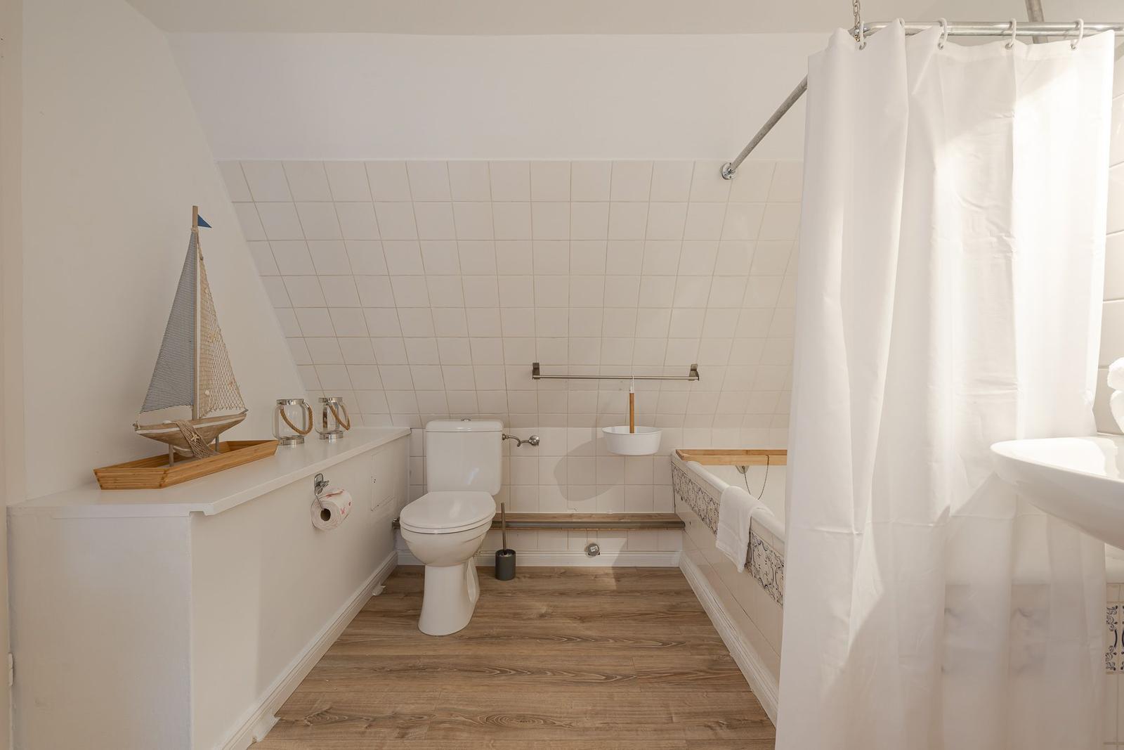 Badezimmer mit Dusche, Toilette und Badewanne. Holzfußboden und weiße Fliesen.