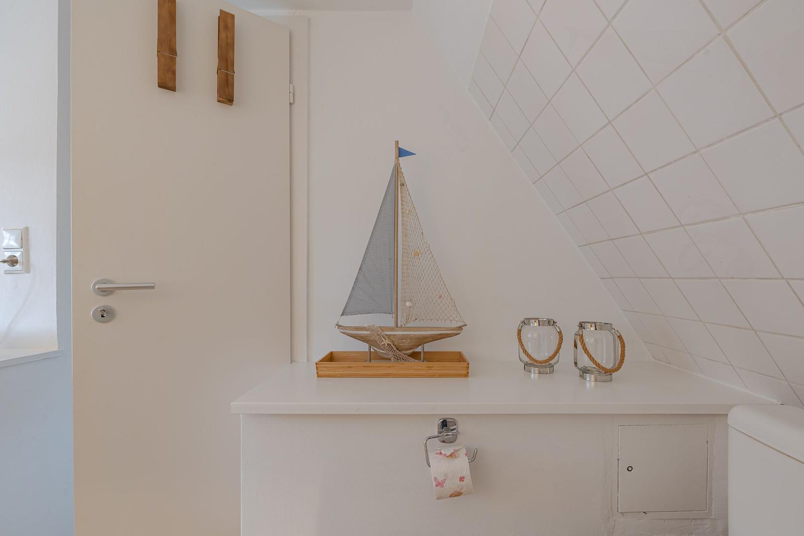 Badezimmer mit Segelschiffmodell und zwei Glasbehältern auf weißem Waschtisch.