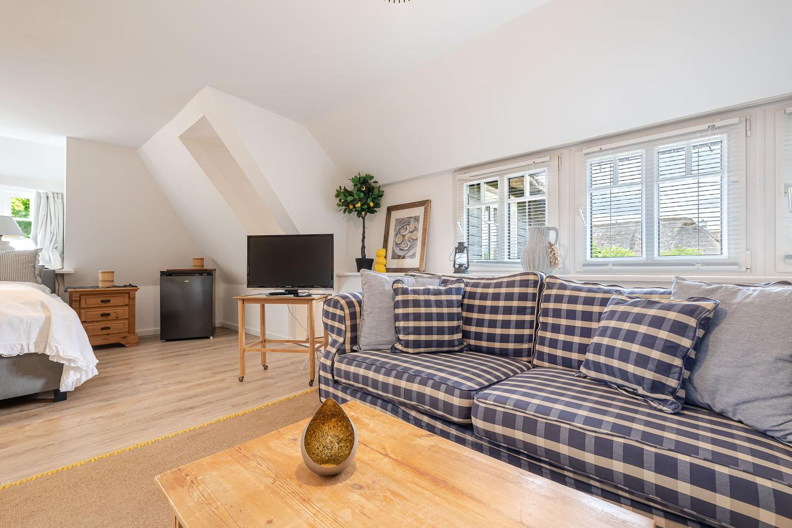 Wohnzimmer mit Sofa, Fernseher und Fenster. Schlafzimmer im Hintergrund.