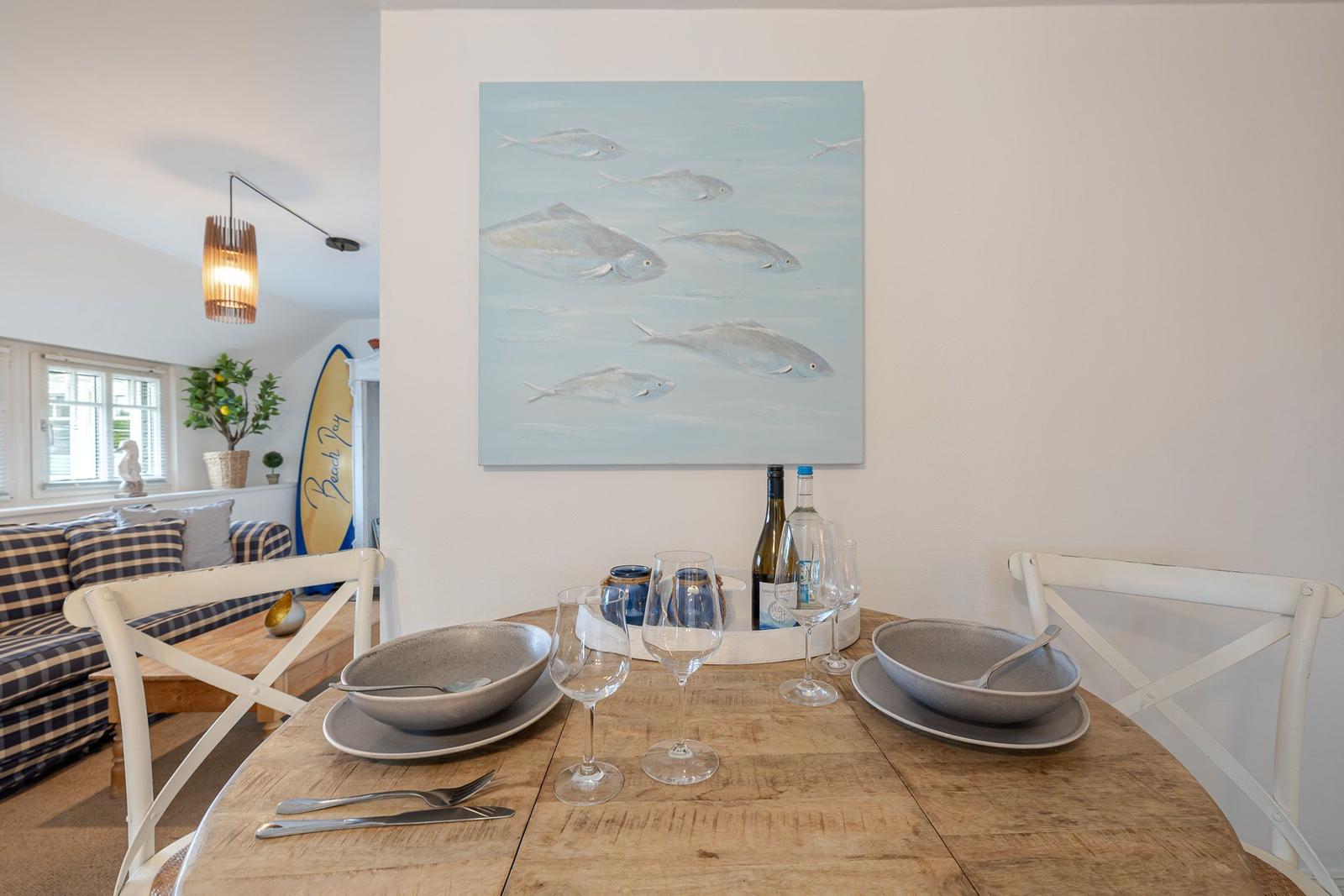 Esstisch mit Geschirr und Wein, Wandbild mit Fischen, Sitzgelegenheit im Hintergrund.