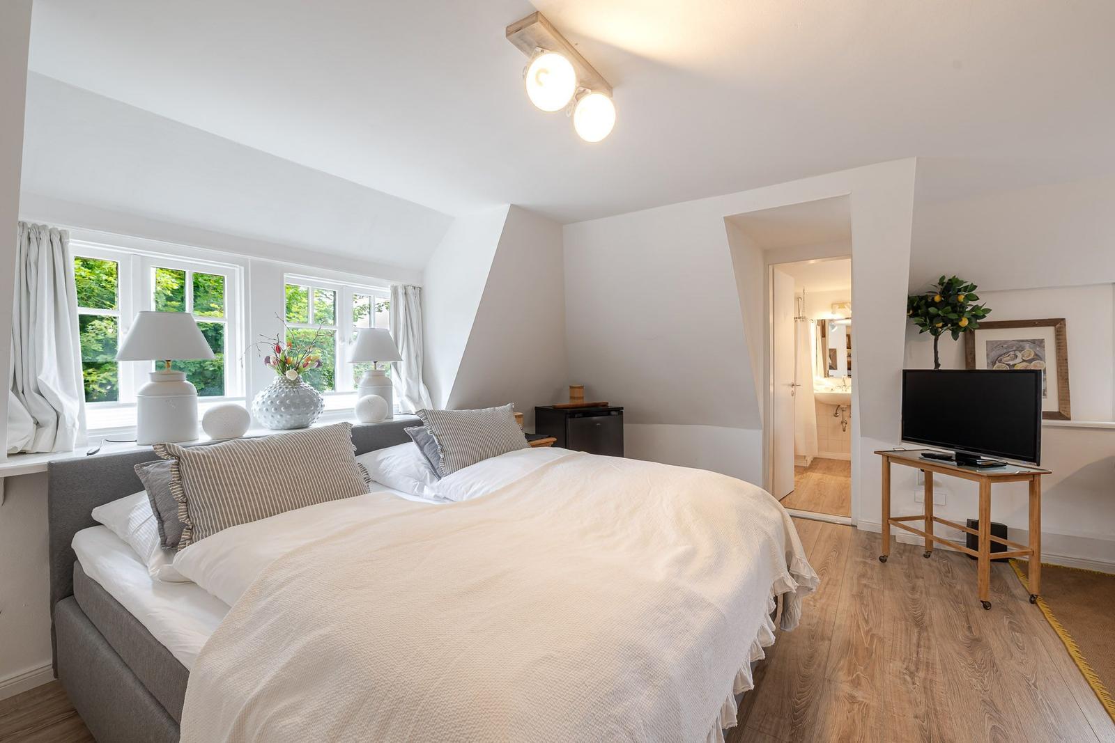 Doppelbett mit weißen Bettwäsche, Fenster mit Blick auf Grün, Fernseher auf Holzständer