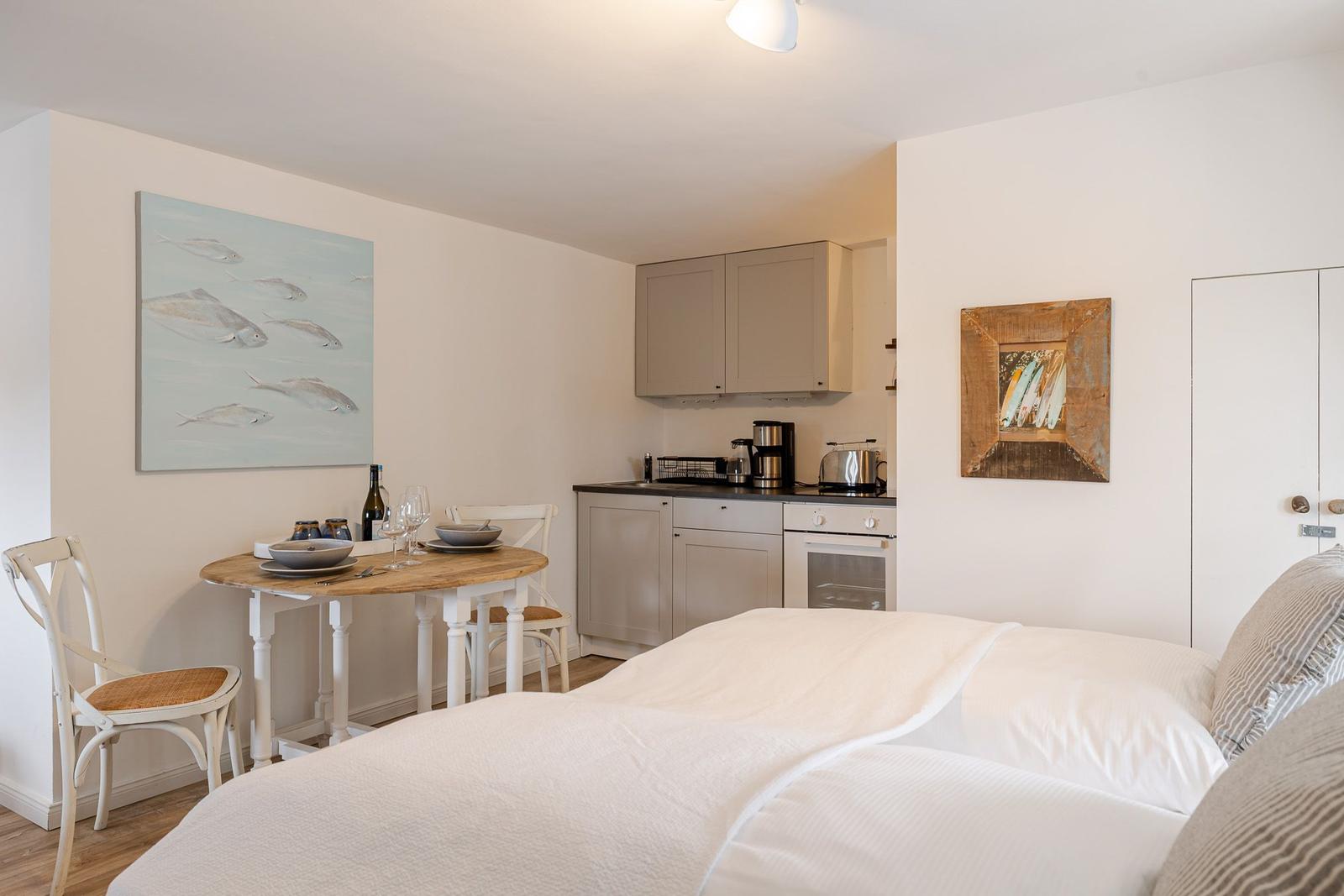 Schlafzimmer mit kleiner Küche und Esstisch. Wandbilder und weiße Wände.