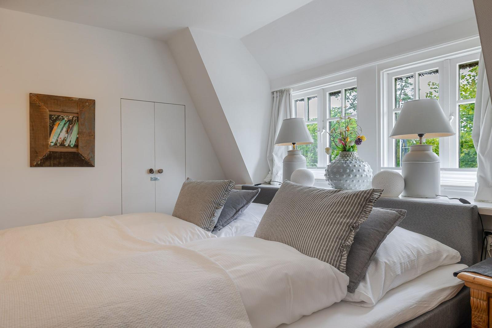 Schlafzimmer mit Dachschrägen, Bett, zwei Nachttische und Fenster mit Blick auf Grün.