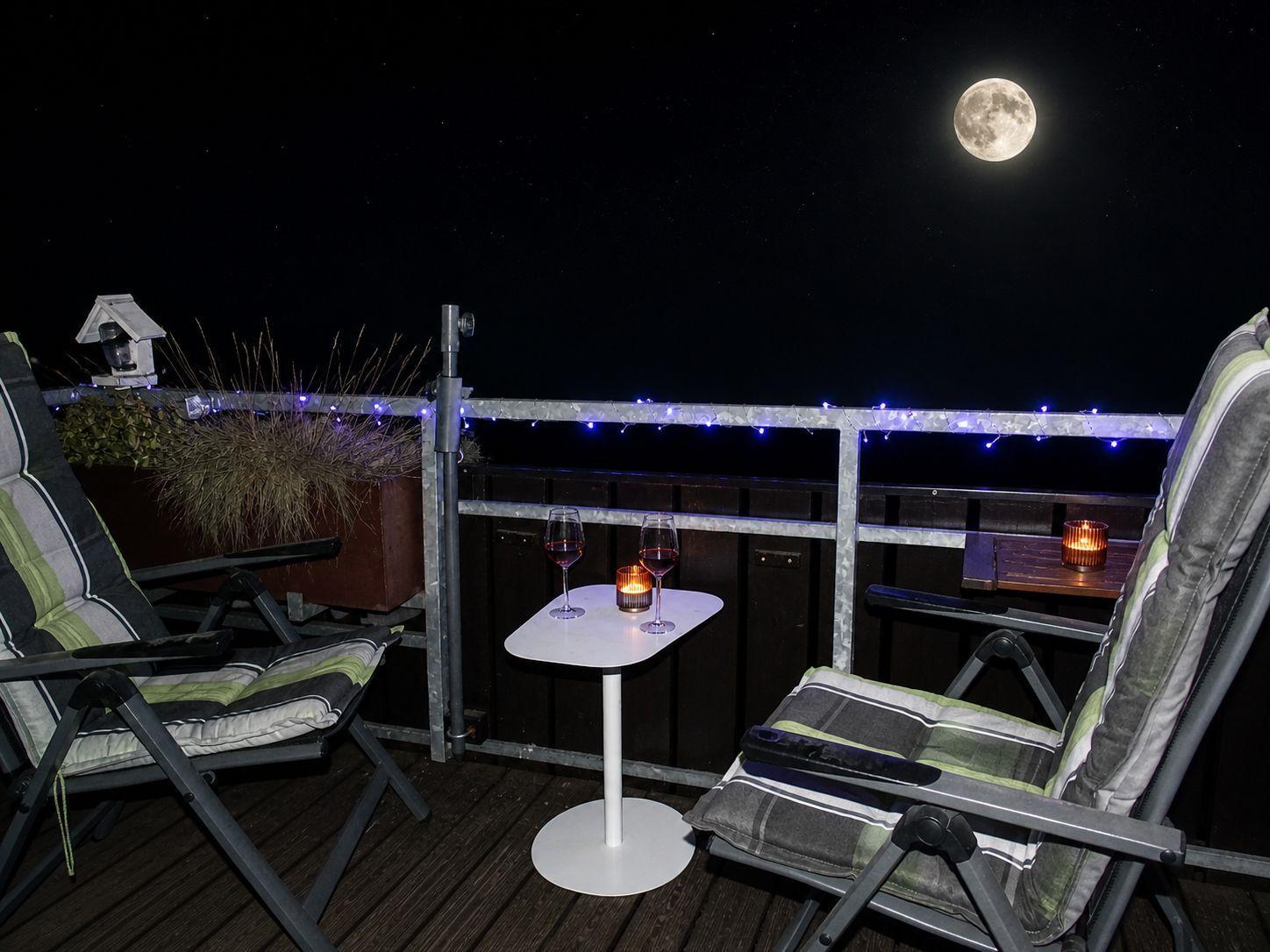 Terrasse mit zwei Stühlen, Tisch, Wein und Kerze unter Vollmond.