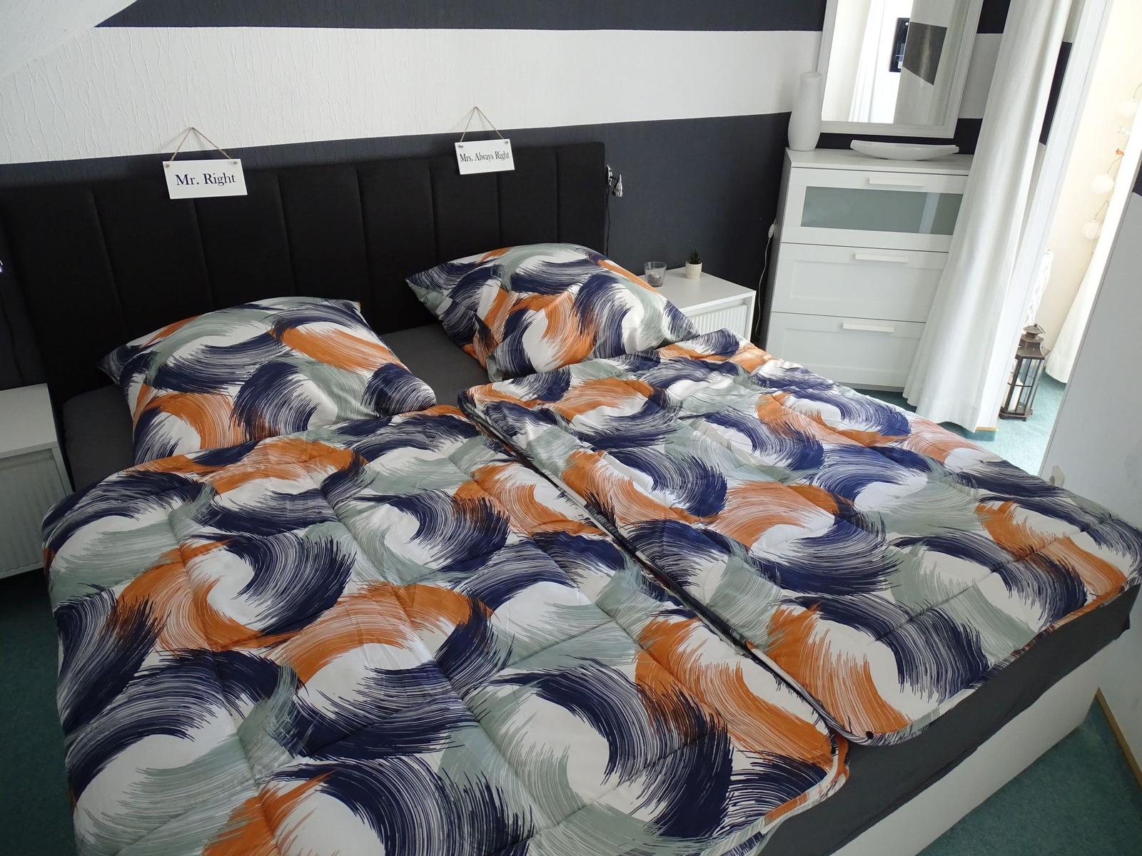 Doppelbett mit gemustertem Bettbezug, Nachttische und Schrank im Schlafzimmer.