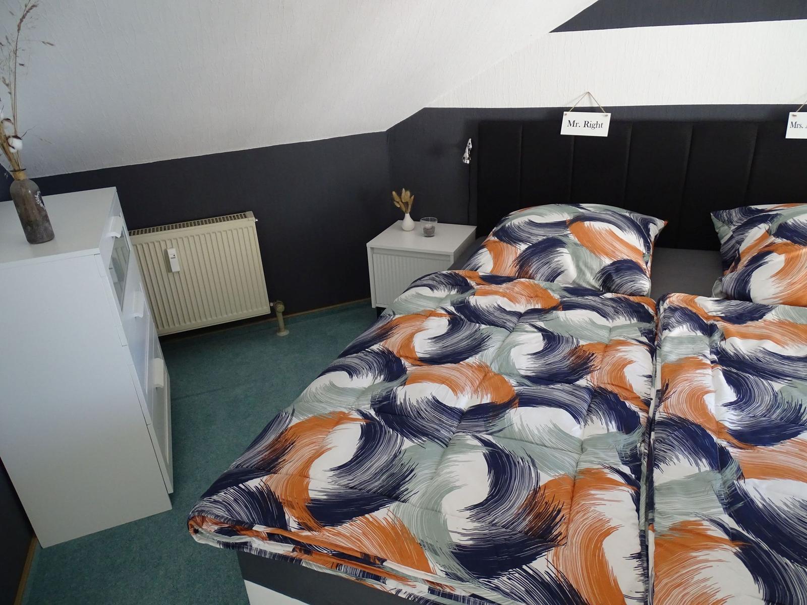 Zwei Betten mit gemustertem Bettzeug, Nachttisch, Schrank und Heizung.