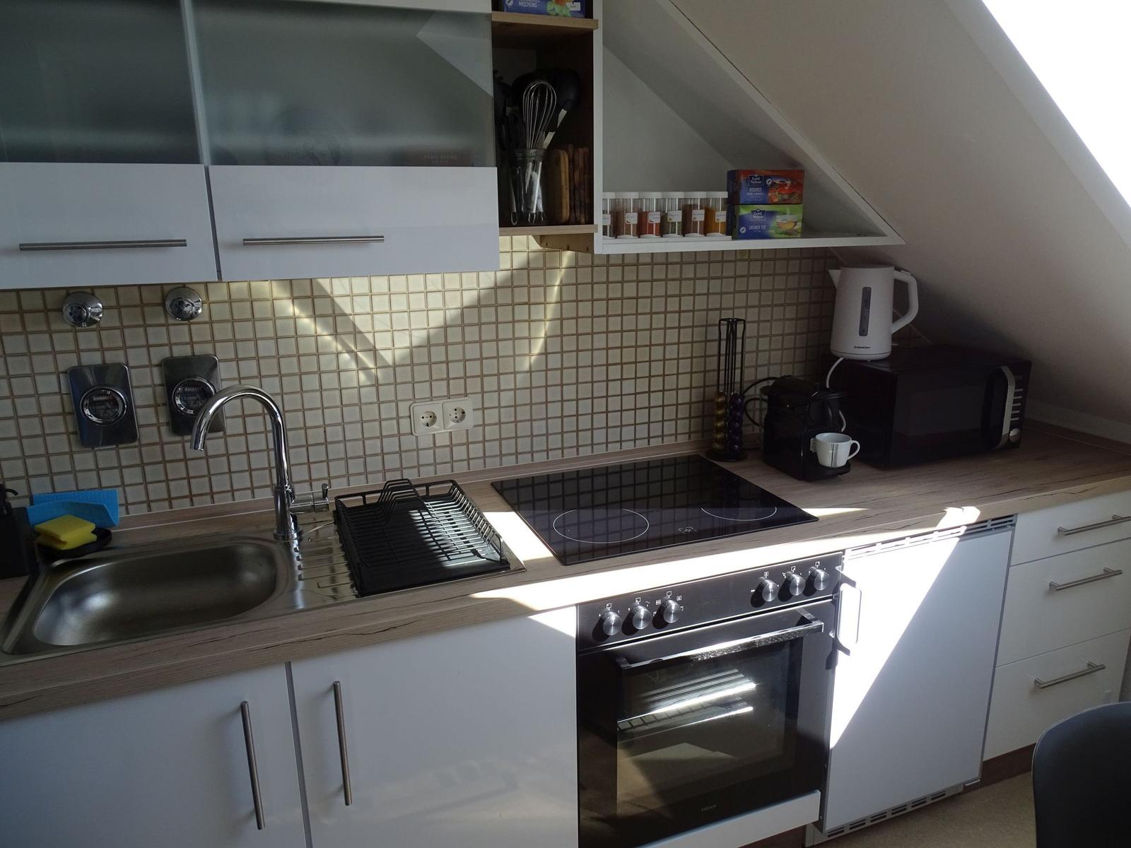 Küche mit Spüle, Herd und Backofen. Auf Arbeitsfläche stehen Mikrowelle und Kaffeemaschine.