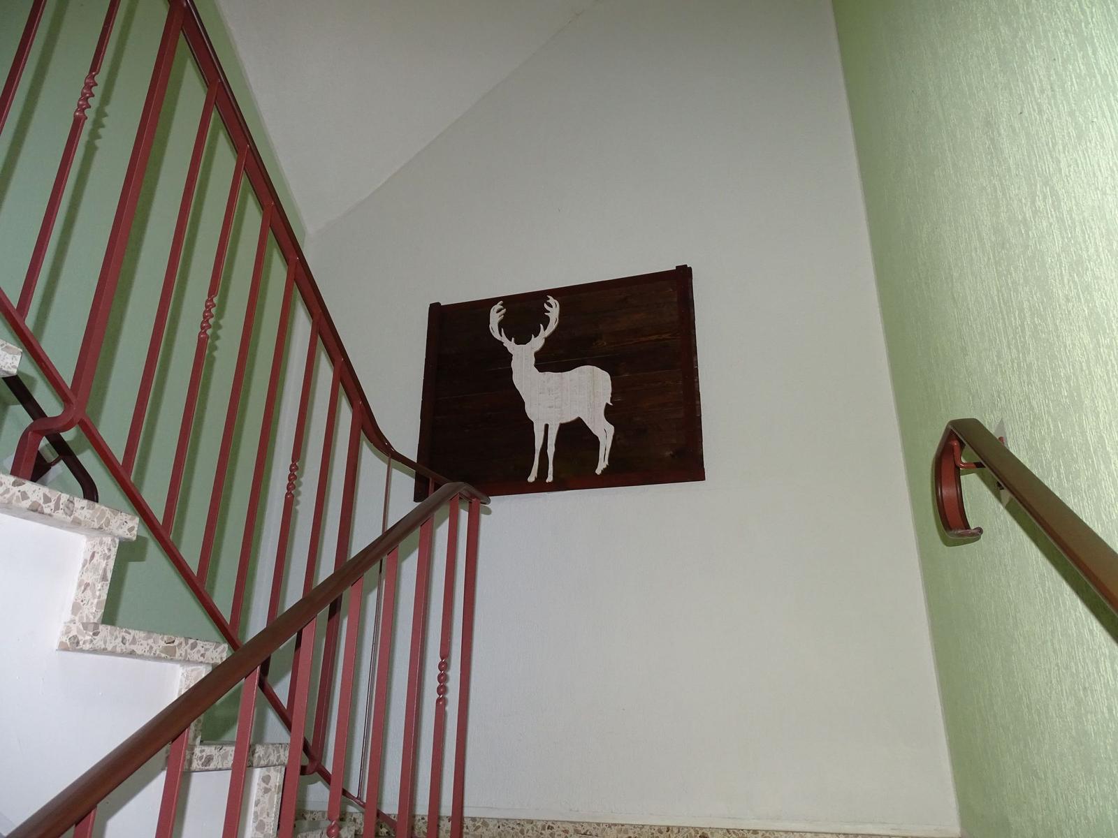 Treppenhaus mit rotem Geländer und Wanddekoration mit Hirschsilhouette.