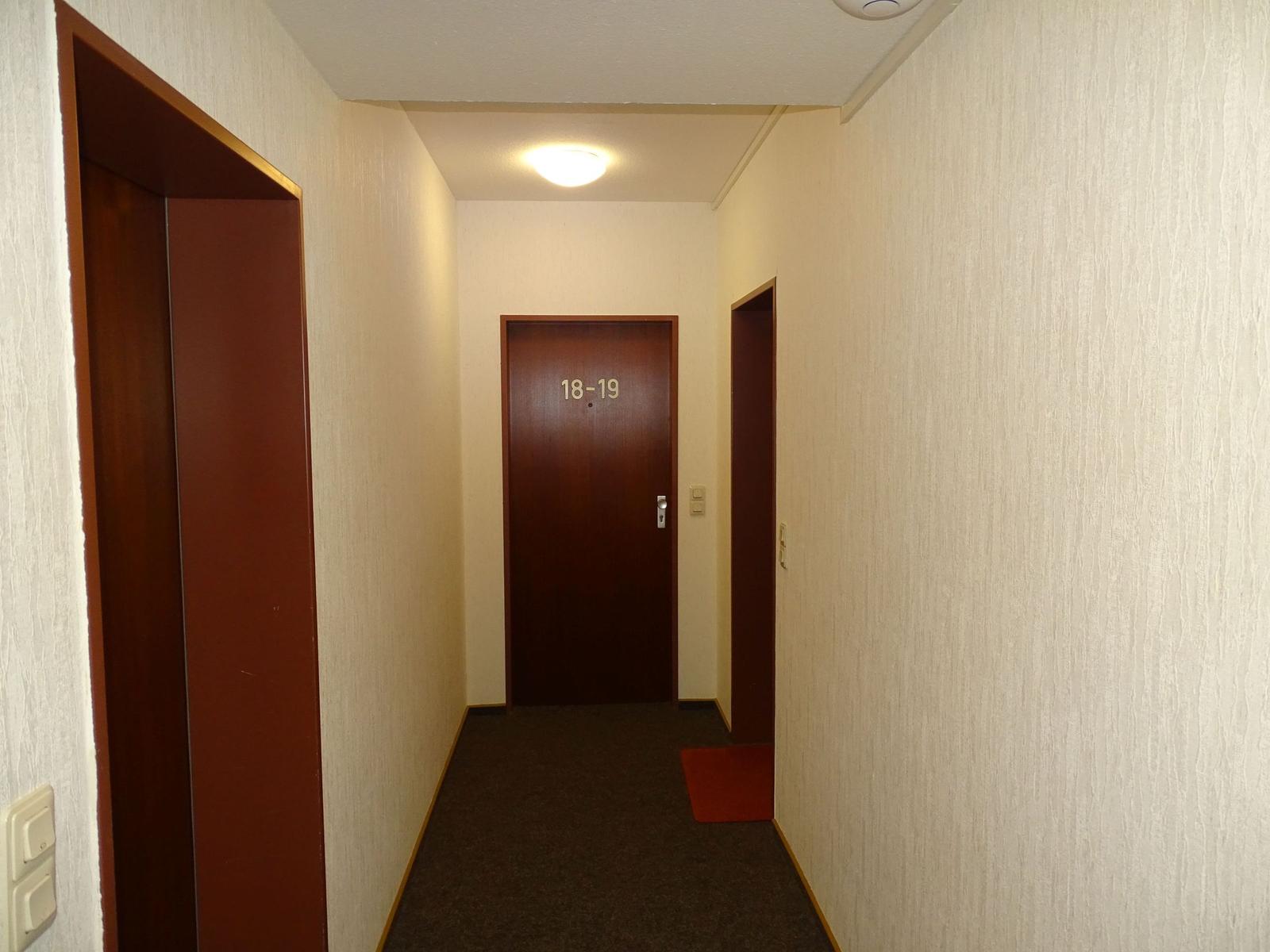 Flur mit Tür 18-19 und zwei weiteren Türen. Teppichboden und hell gestrichene Wände.