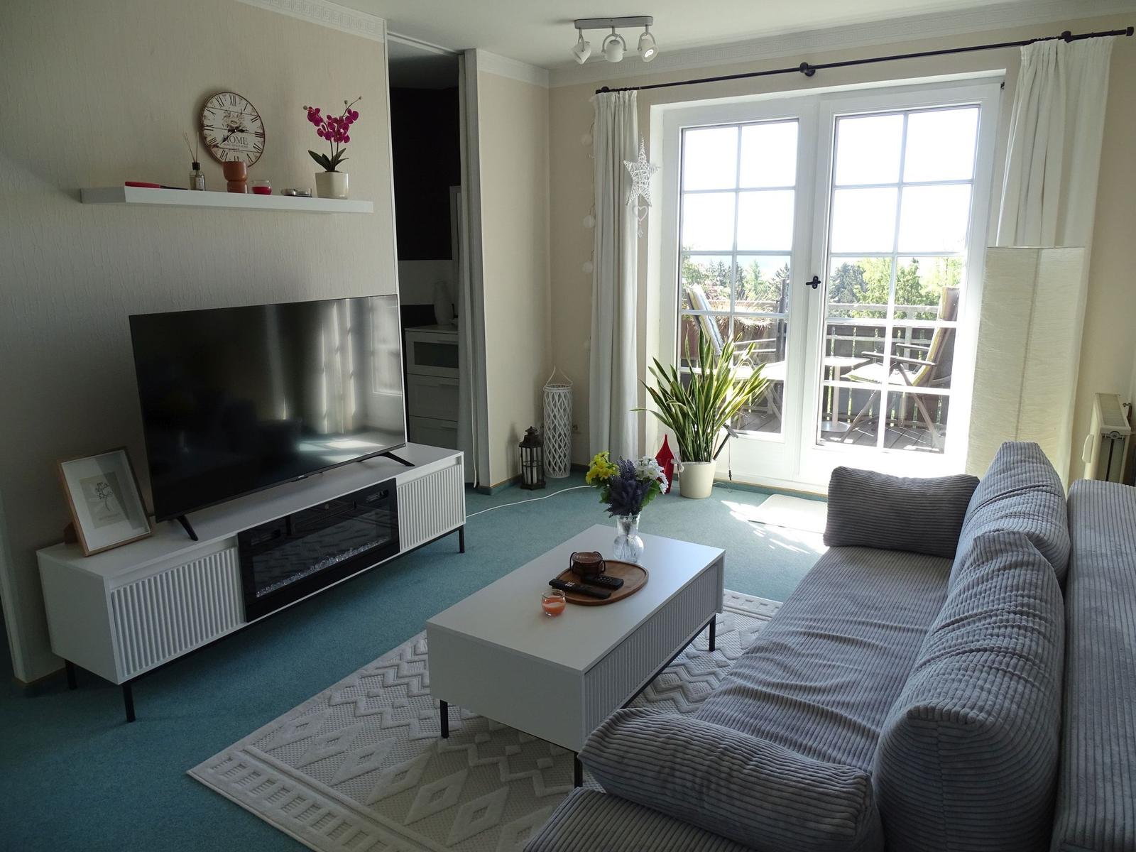 Wohnzimmer mit Sofa, Fernseher und Balkonzugang.
