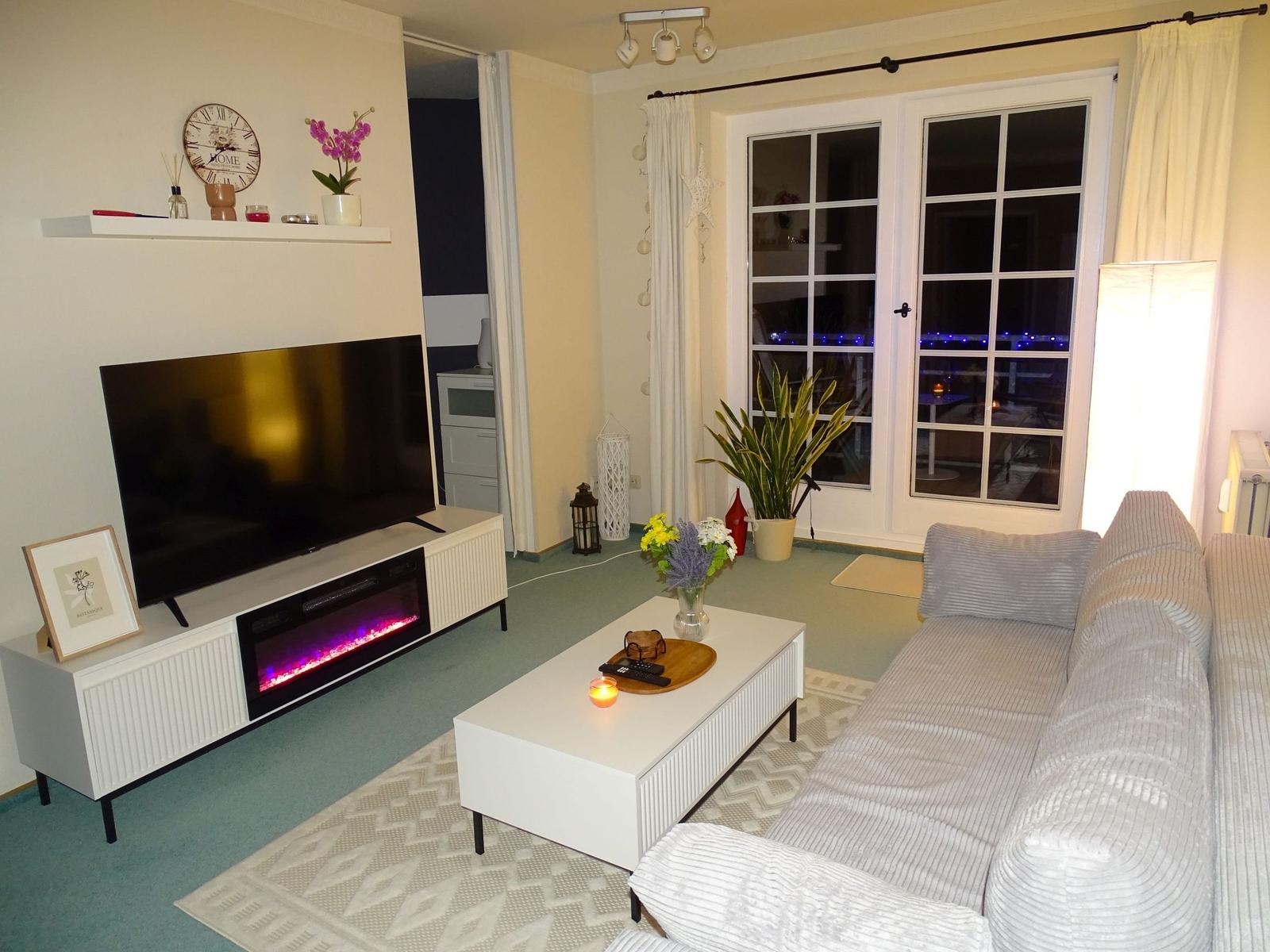 Wohnzimmer mit Sofa, Fernseher und elektrischem Kamin.