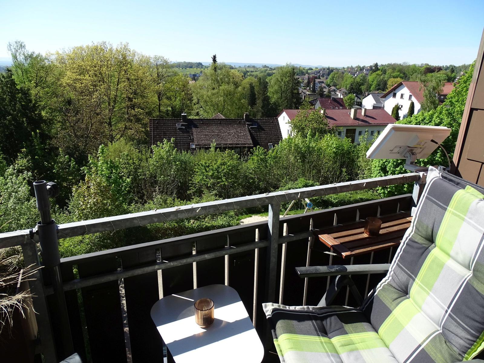 Balkon mit Sitzgelegenheit und Blick auf grüne Landschaft und Häuser