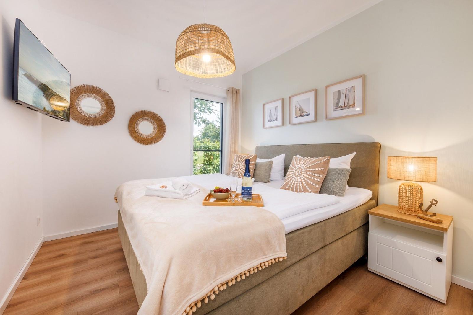 Schlafzimmer mit Bett, Fernseher und Fenster zur Außenterrasse.