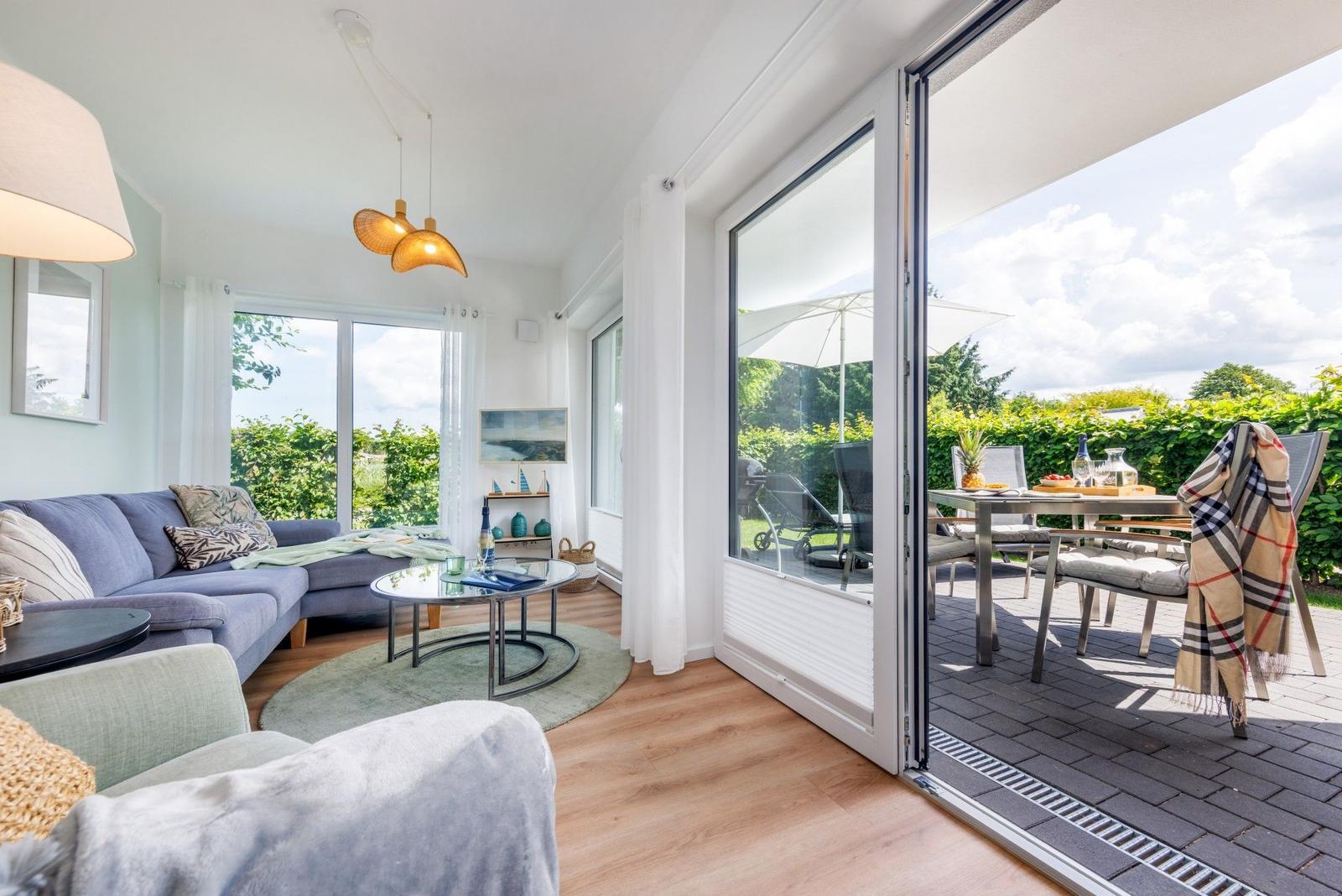 Wohnzimmer mit Sofa, Couchtisch und Terrasse mit Tisch, Stühlen und Sonnenschirm.