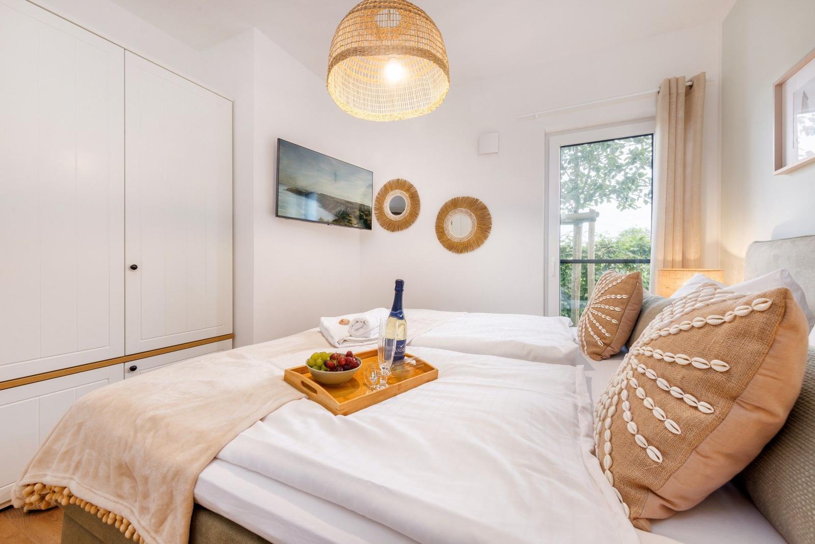 Schlafzimmer mit Bett, Schrank und Fenster. Auf dem Bett steht ein Tablett mit Obst und Wein.