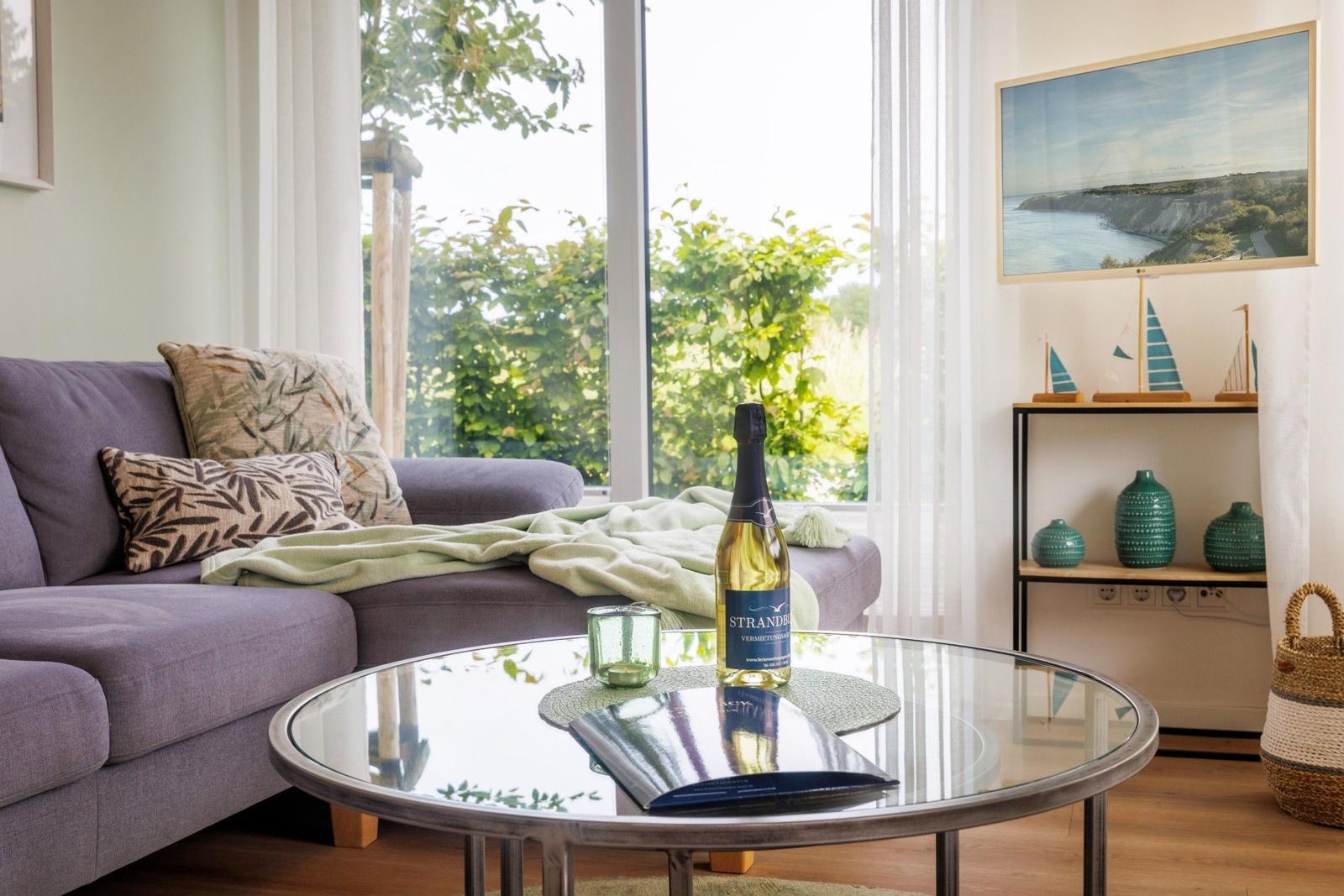 Lounge mit Sofa, Glas-Tisch und Blick auf grüne Bäume.